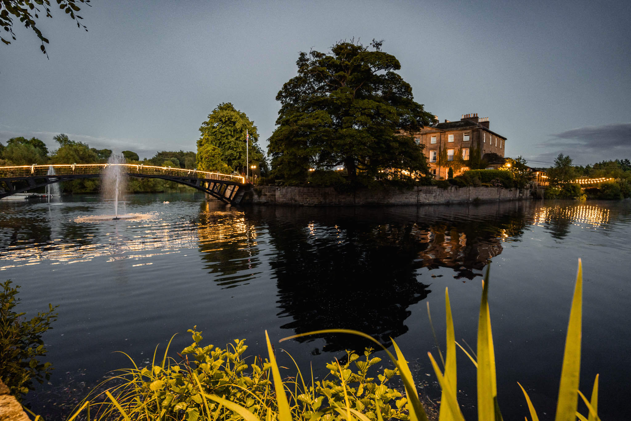A beautifully illuminated historic wedding venue at night, reflecting on a serene lake, creating a magical and romantic atmosphere.