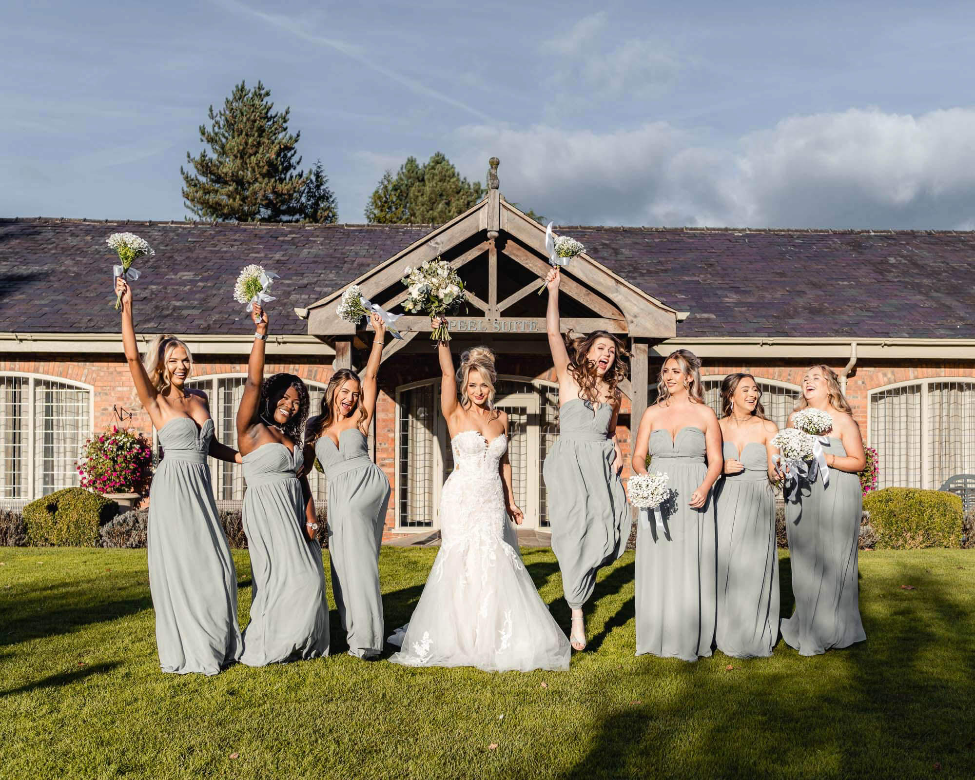 A joyful bride with her bridesmaids in matching sage-green dresses, celebrating together outdoors on a sunny wedding day.