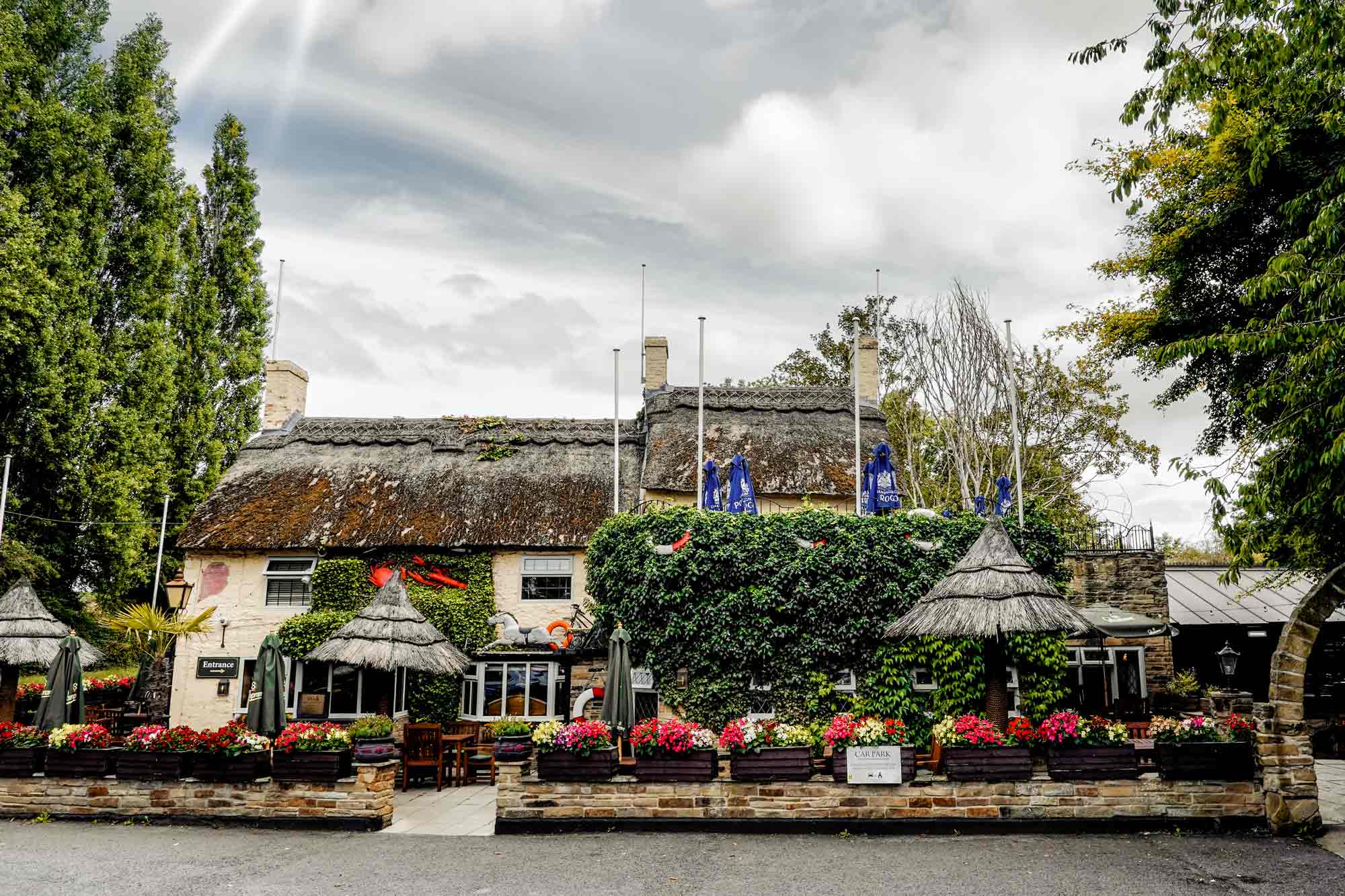 Front view of Crab & Lobster Hotel & Restaurant in Asenby, North Yorkshire, with thatched roof, ivy-covered walls, and vibrant floral displays.
