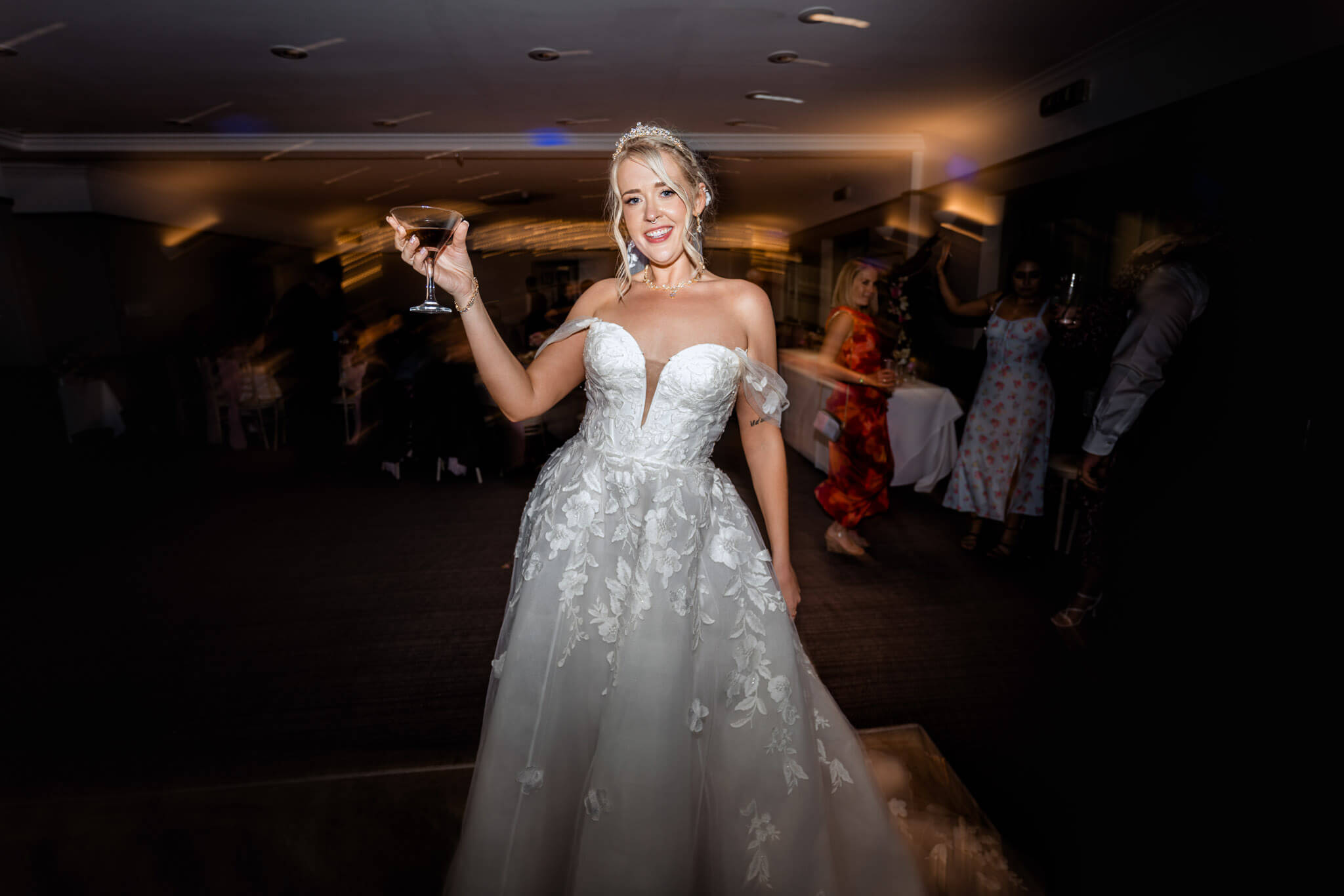 Bride in lace wedding gown holding a champagne glass on the dance floor.