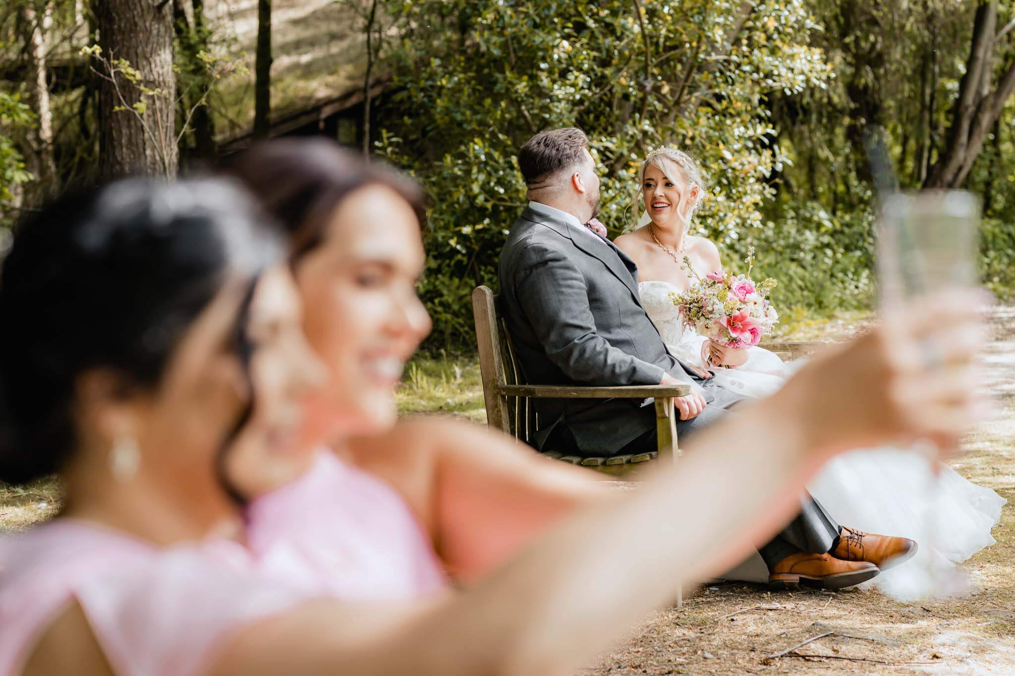 Bride and groom smiling at each other on a wooden bench at Chevin Country Park Hotel.