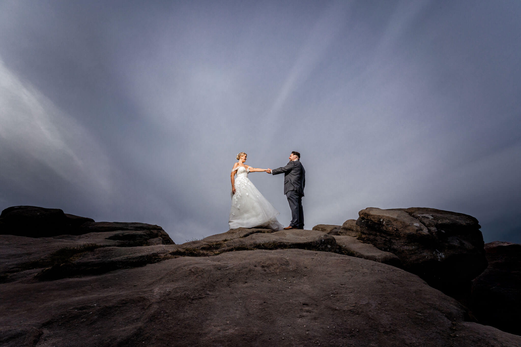 Bride and groom holding hands on dramatic rocks at Surprise View Otley.