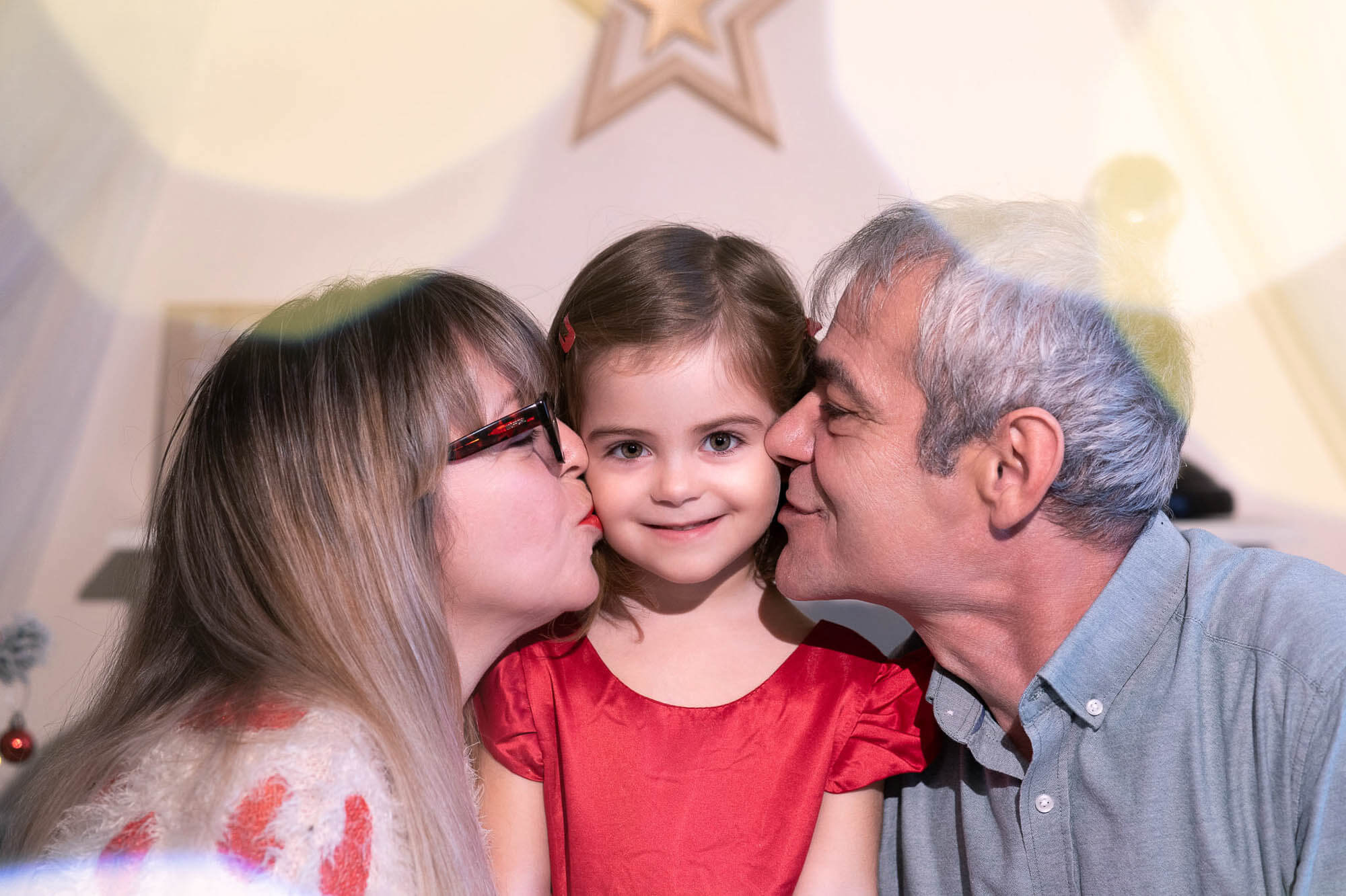Grandparents kissing smiling granddaughter during family festive session at Calini Weddings Studio.