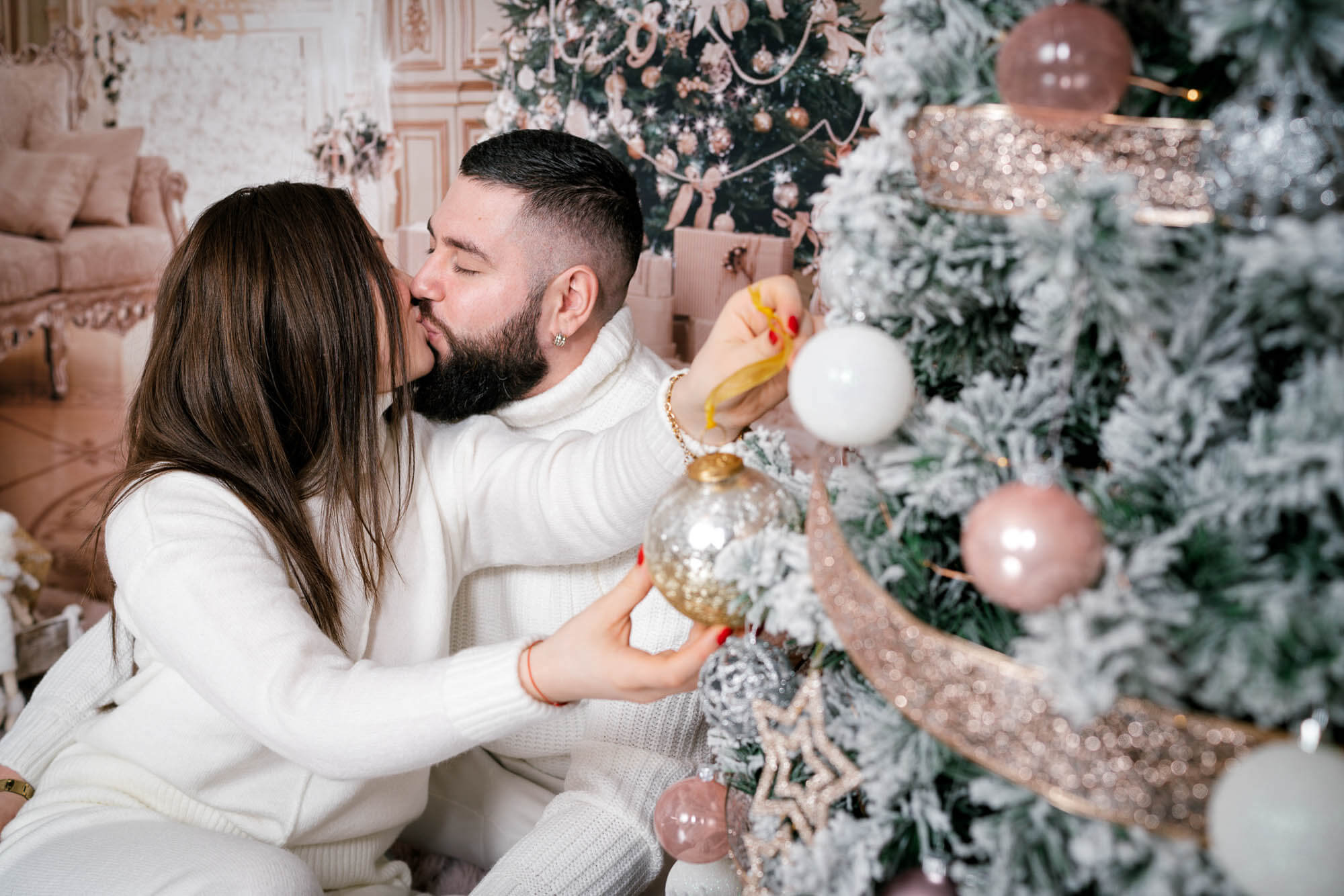 Couple kissing while hanging ornaments during Christmas photoshoot in Calini Weddings Studio.