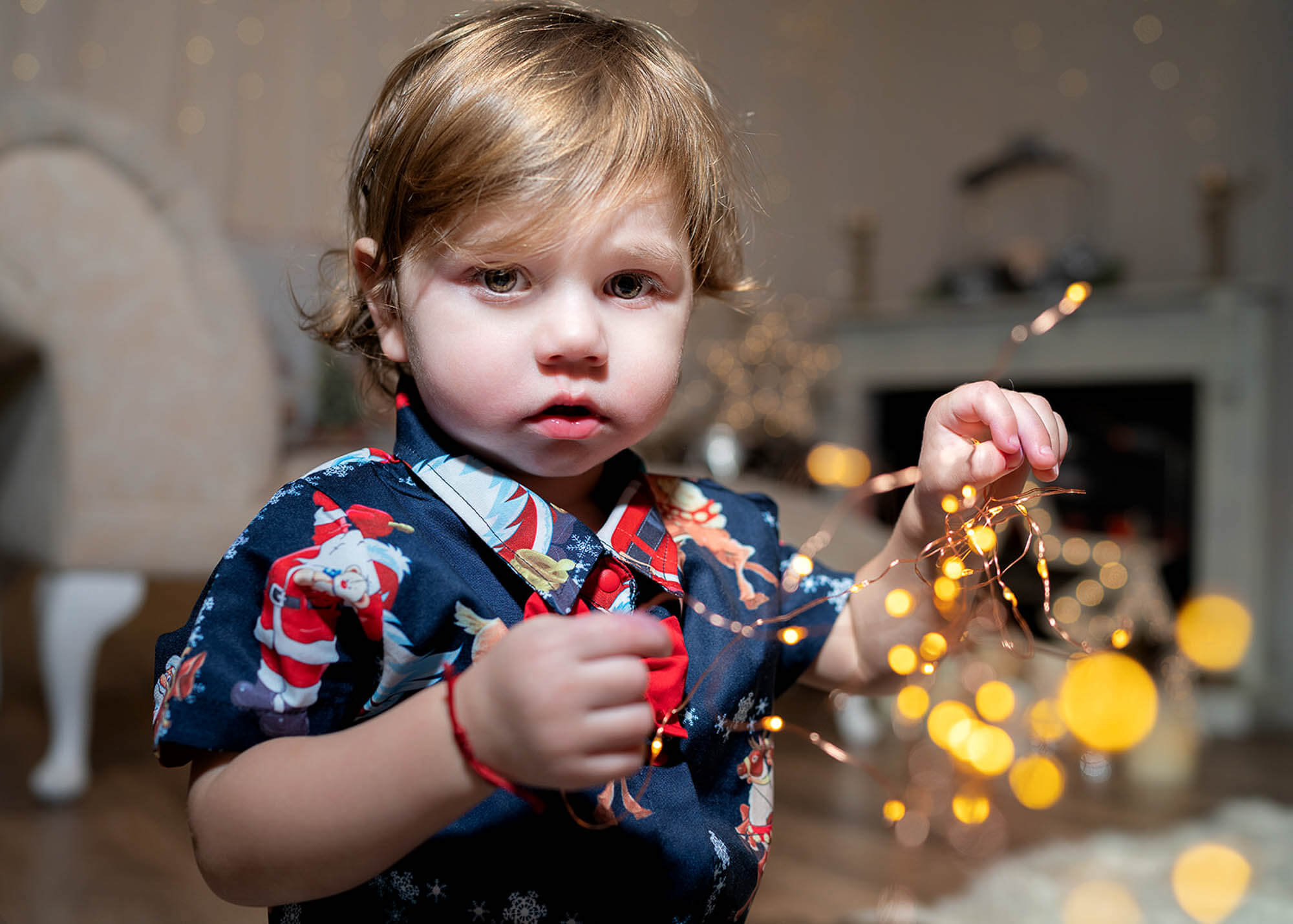 Little boy holding golden fairy lights during cozy behind-the-scenes Christmas mini session.