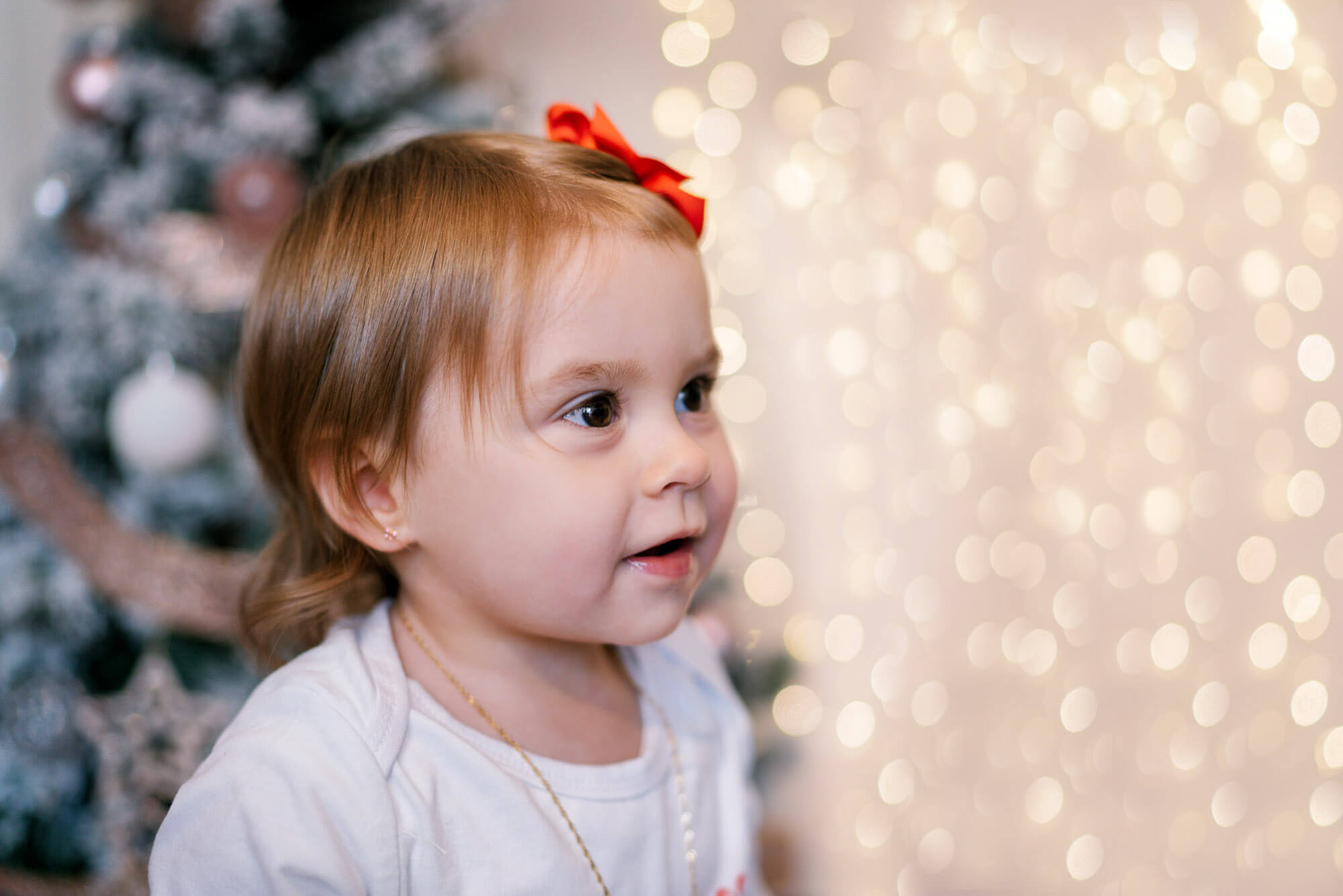Baby girl smiling beside decorated tree during behind-the-scenes festive session in Leeds.