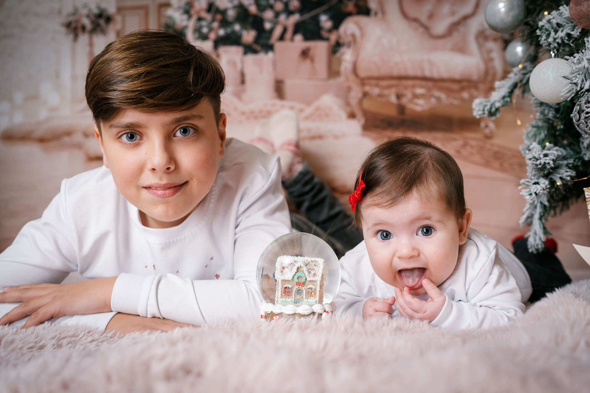 Brother and baby sister smiling near Christmas tree – behind-the-scenes studio moment captured in Leeds.