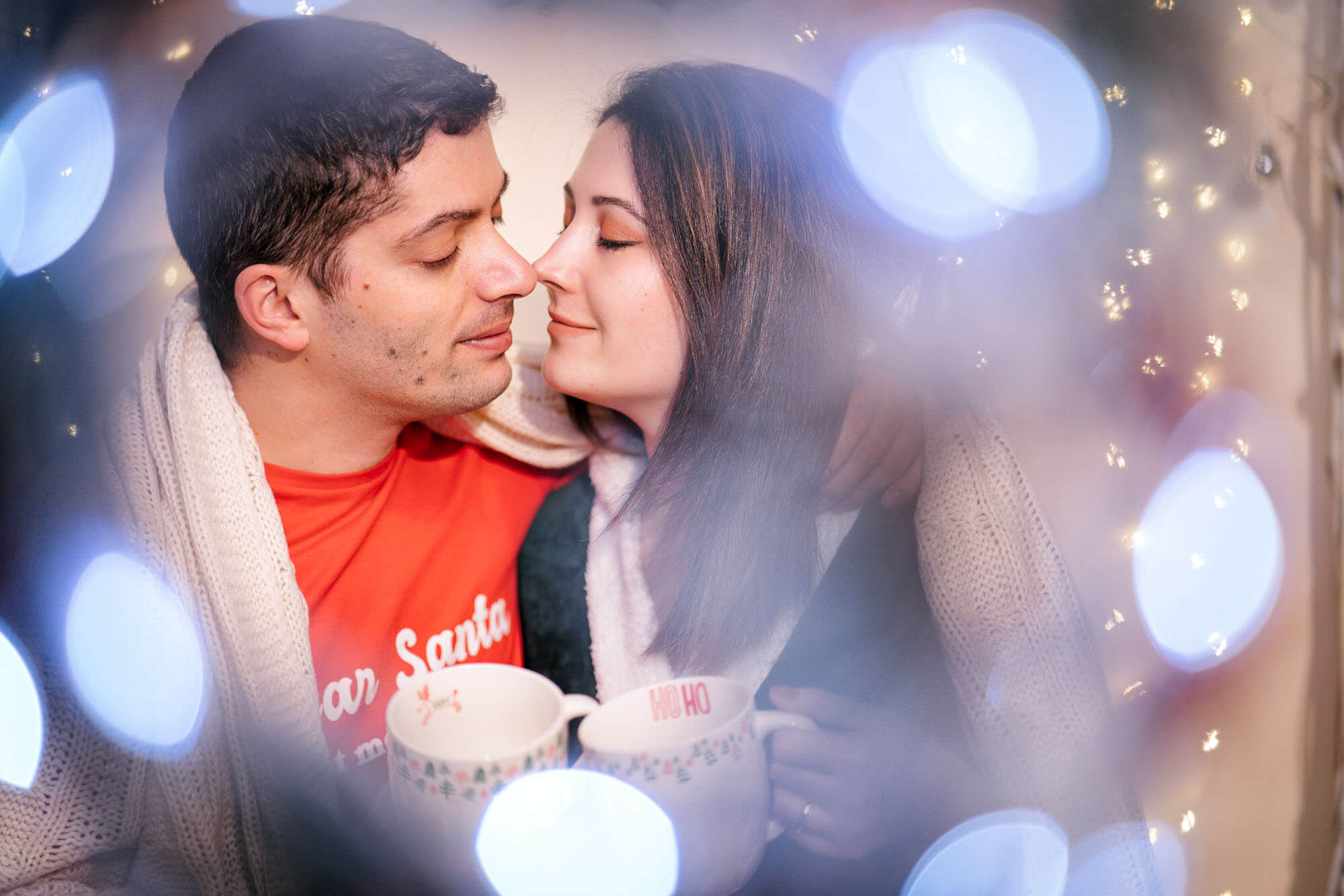 Couple cuddling with festive mugs surrounded by warm lights during Christmas studio shoot in Leeds.
