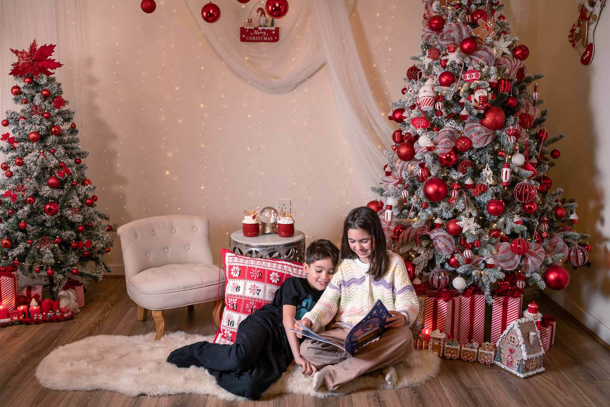 Brother and sister reading book near Christmas tree during behind-the-scenes photo session in Yorkshire.