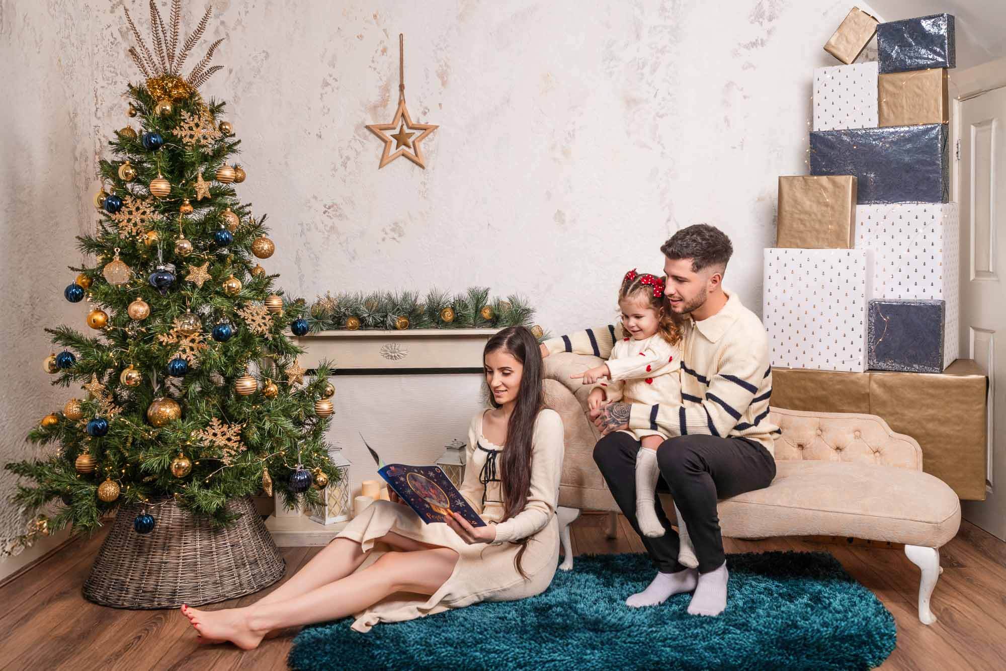Family reading book beside gold and navy Christmas tree during Leeds behind-the-scenes photo session.