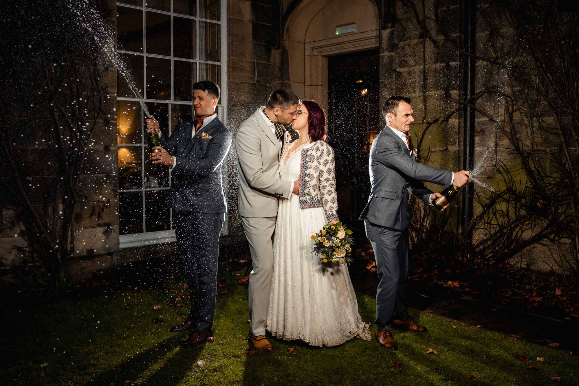 Bride and groom celebrating their wedding at Swinton Estate Yorkshire as groomsmen spray champagne outside the historic venue.