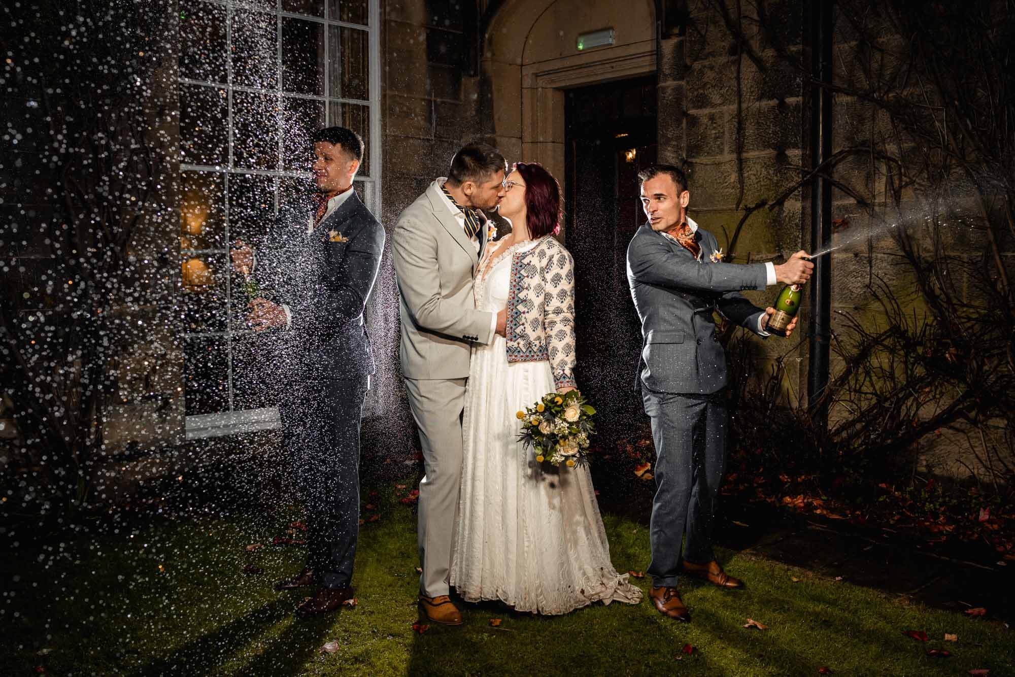 Wedding at Swinton Estate Yorkshire - couple kissing under champagne spray during nighttime celebration with friends at Swinton Estate Yorkshire.