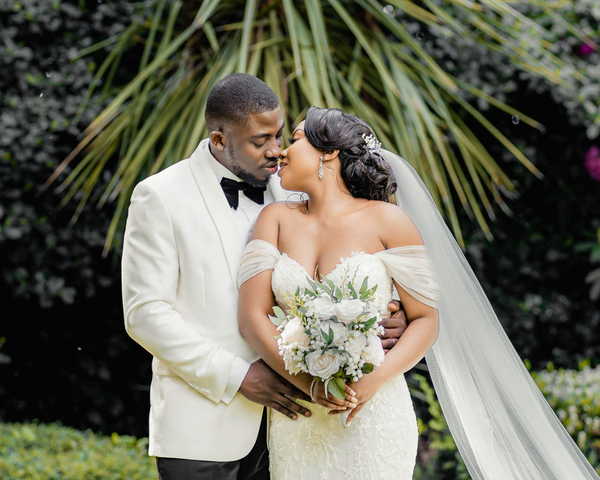 Romantic wedding portrait of an elegant Black couple surrounded by lush greenery.