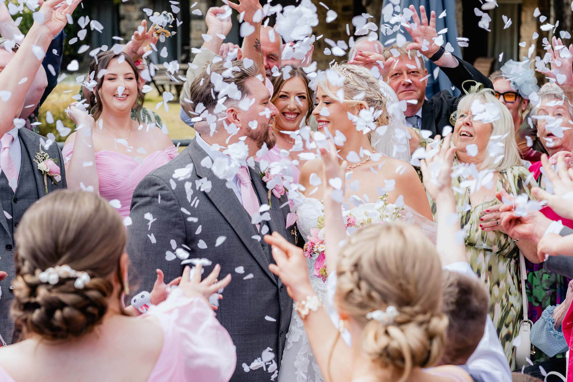 Bride and groom surrounded by guests throwing confetti during a joyful wedding celebration.