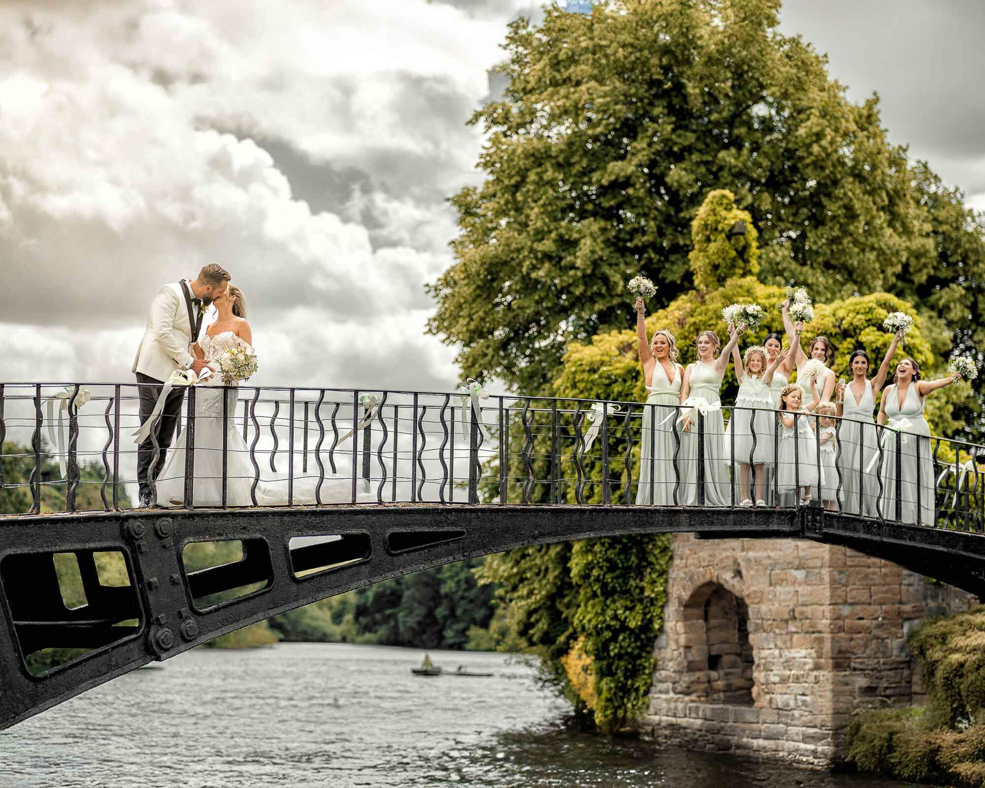 Bride and groom with their bridesmaids celebrating on a bridge during an outdoor wedding.