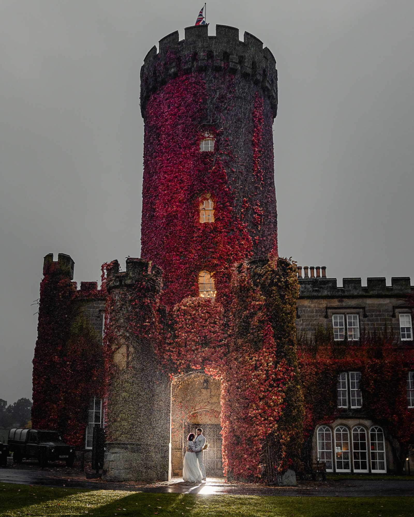 Romantic elopement wedding in Yorkshire as the couple embrace beneath an ivy-covered castle tower in the rain.
