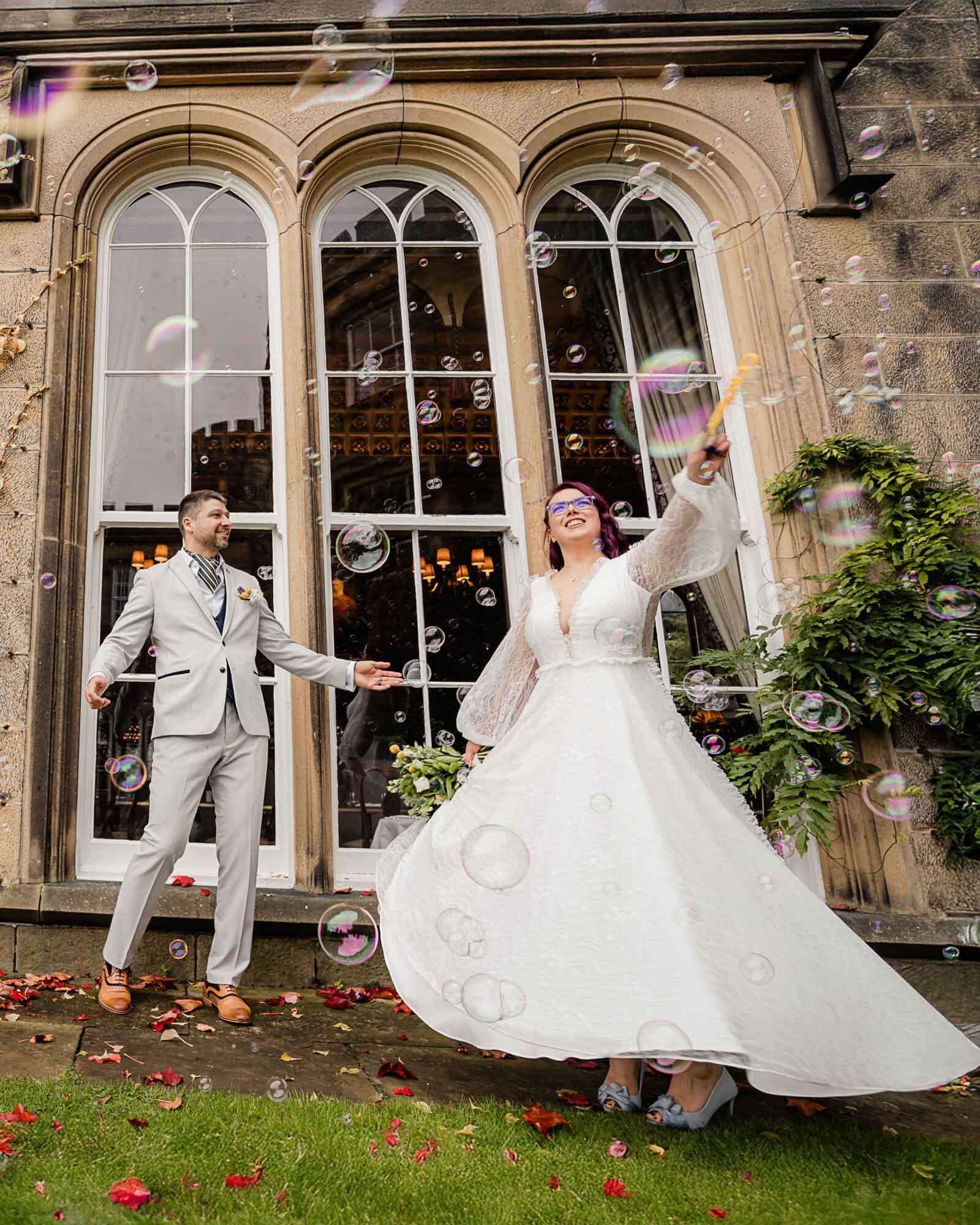 Joyful elopement wedding in Yorkshire as the bride twirls her dress while the couple celebrate with bubbles outside a historic venue.