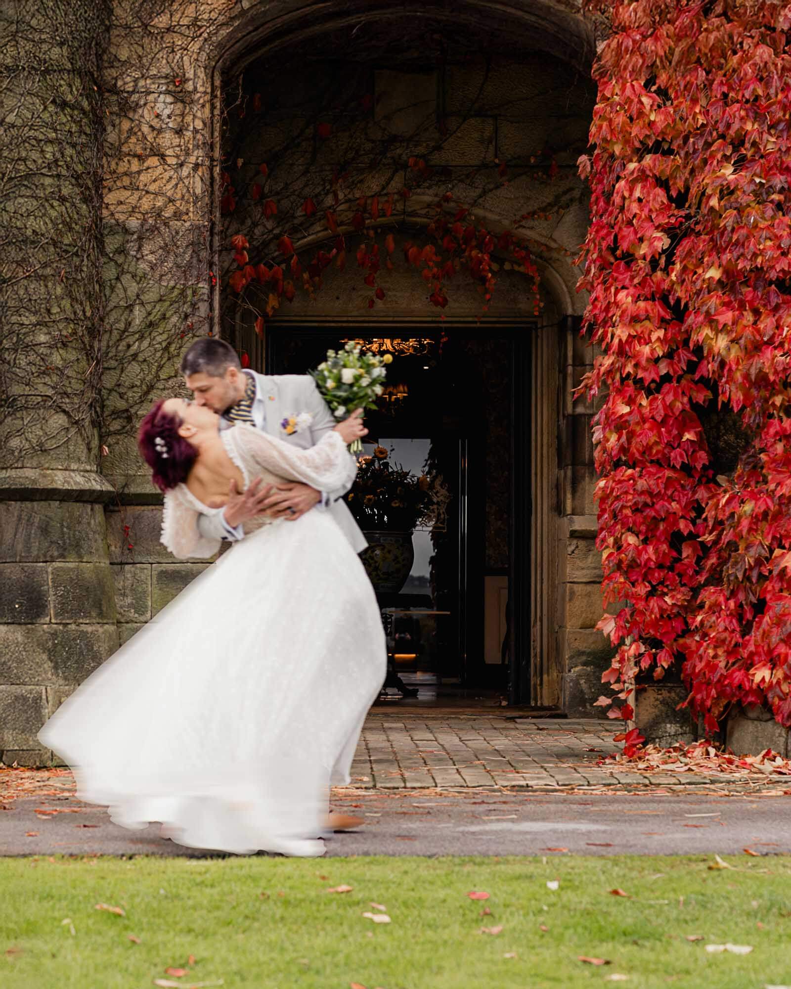 Romantic elopement wedding in Yorkshire as the couple share a kiss beneath an ivy-covered stone archway in autumn.