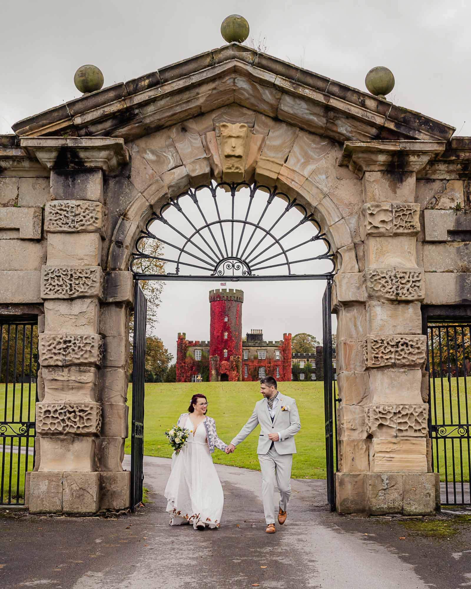 Elopement wedding in Yorkshire as the couple walk hand in hand through a historic stone archway with a castle in the background.