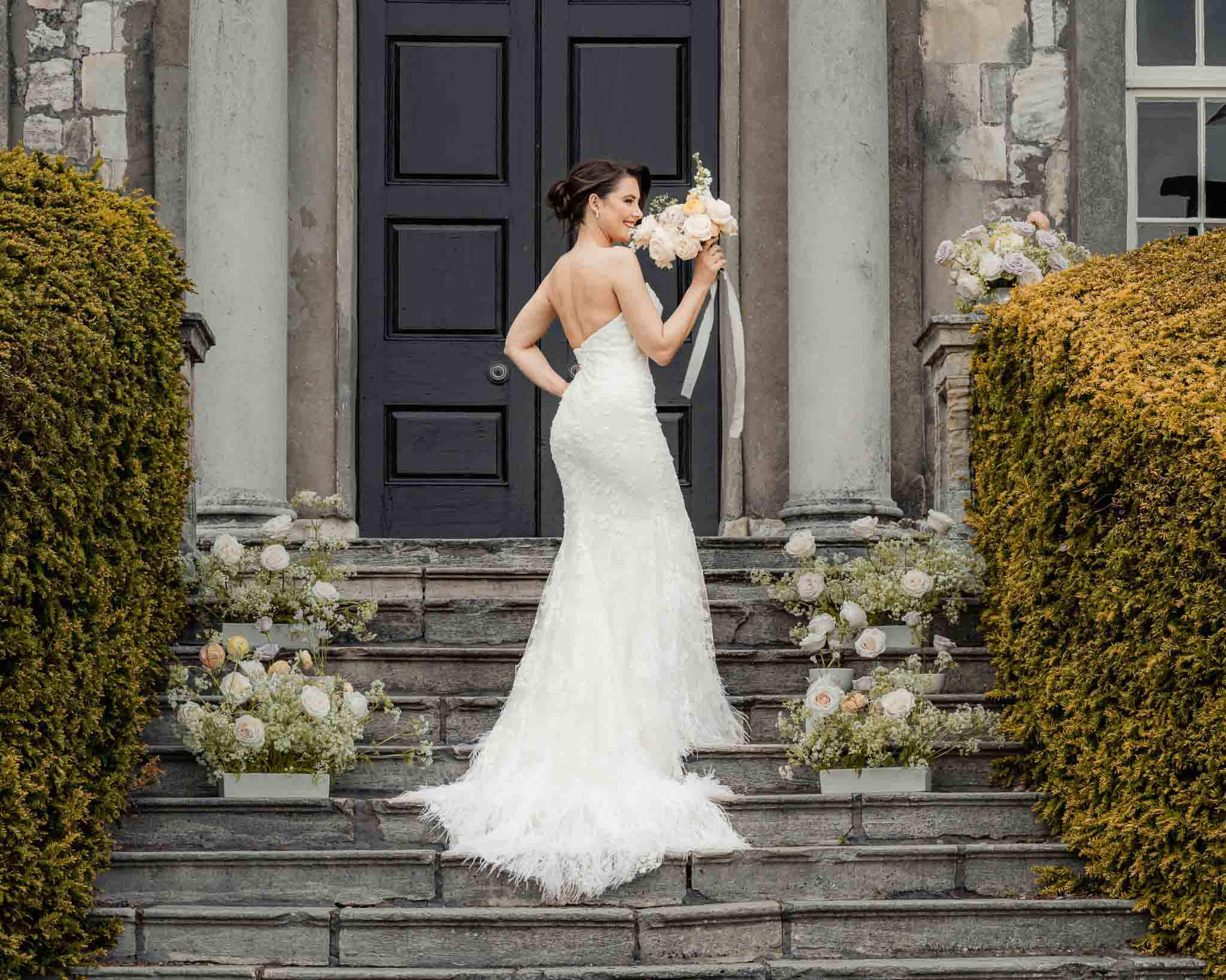 Bride standing on the stone steps outside Hazlewood Castle holding her bouquet