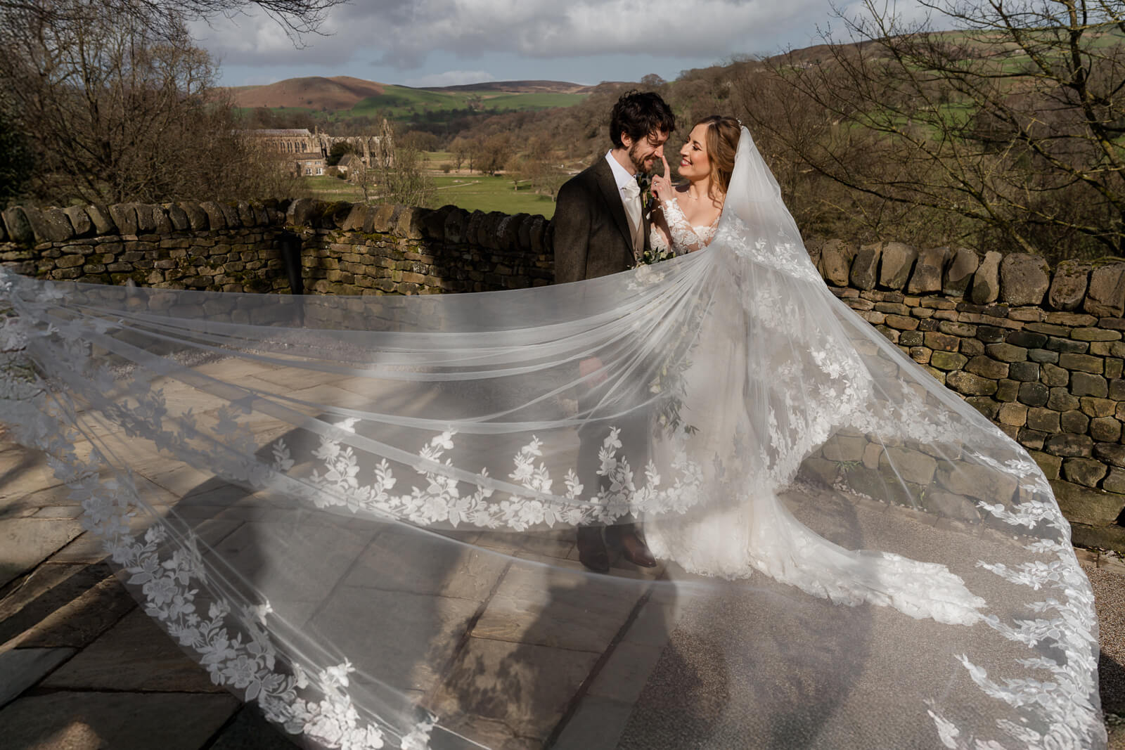 Bride and groom portrait with flowing veil in countryside wedding setting