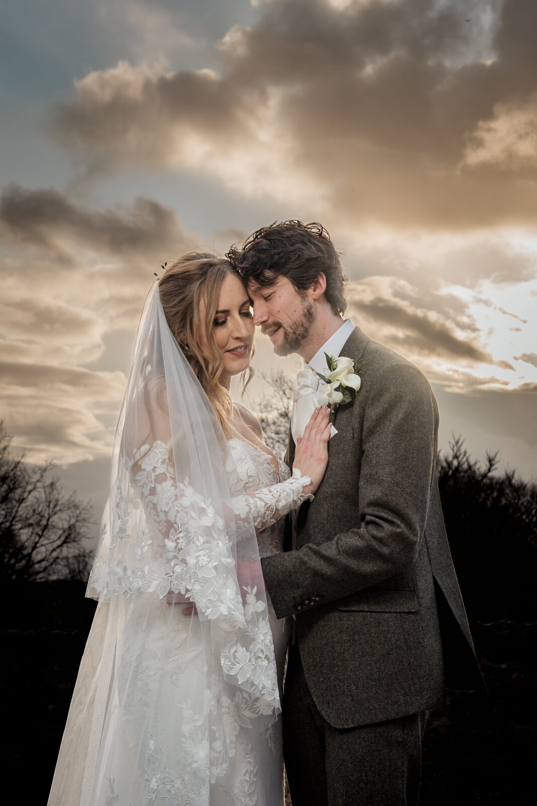 Romantic golden hour portrait of a bride and groom embracing under a dramatic sky during their wedding day