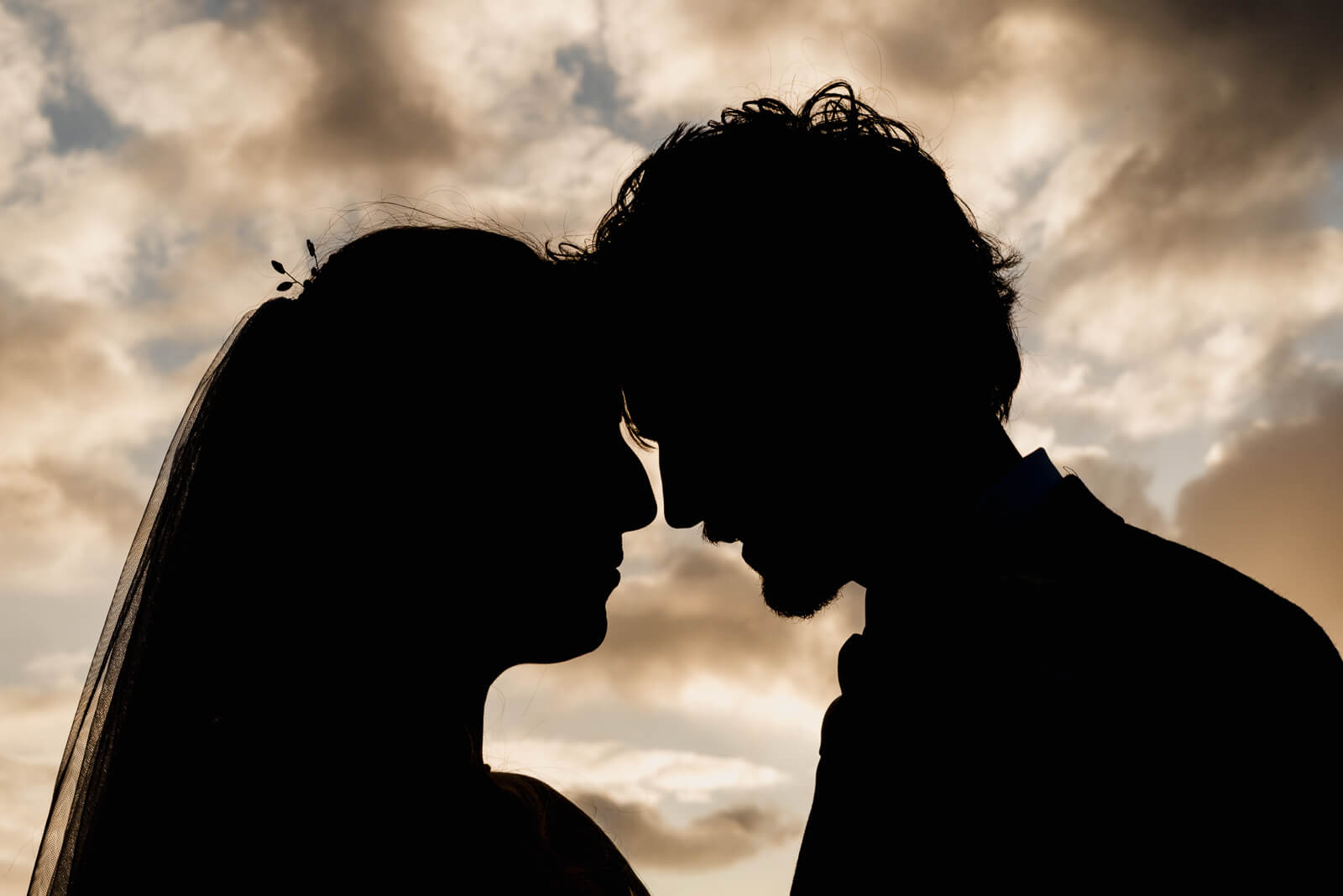 Silhouette of a bride and groom touching foreheads against a dramatic sunset sky during an intimate wedding moment