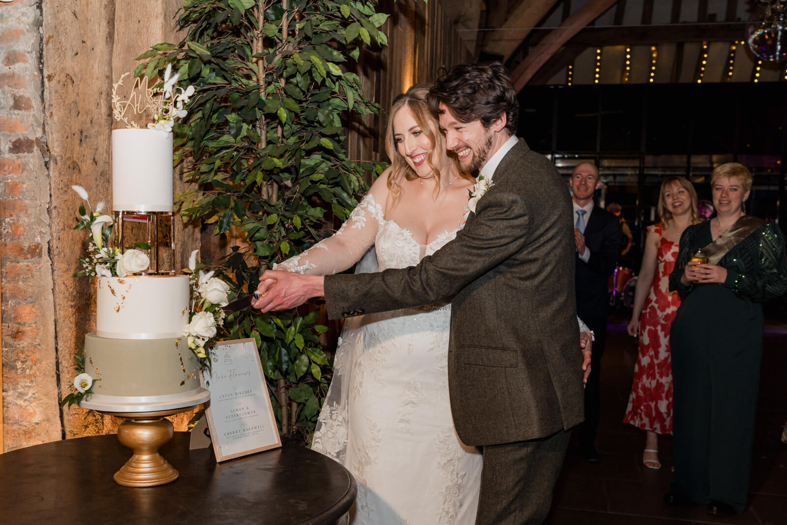 Bride and groom cutting their wedding cake together during an indoor reception with guests watching