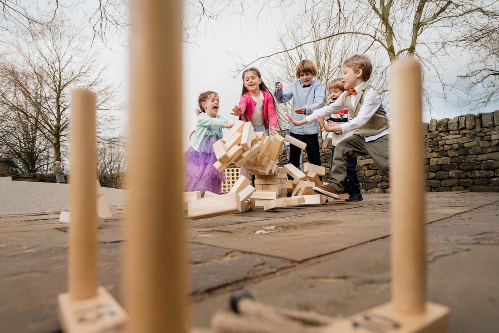 Children playing outdoor lawn games at a wedding, laughing as wooden blocks tumble during a fun candid moment