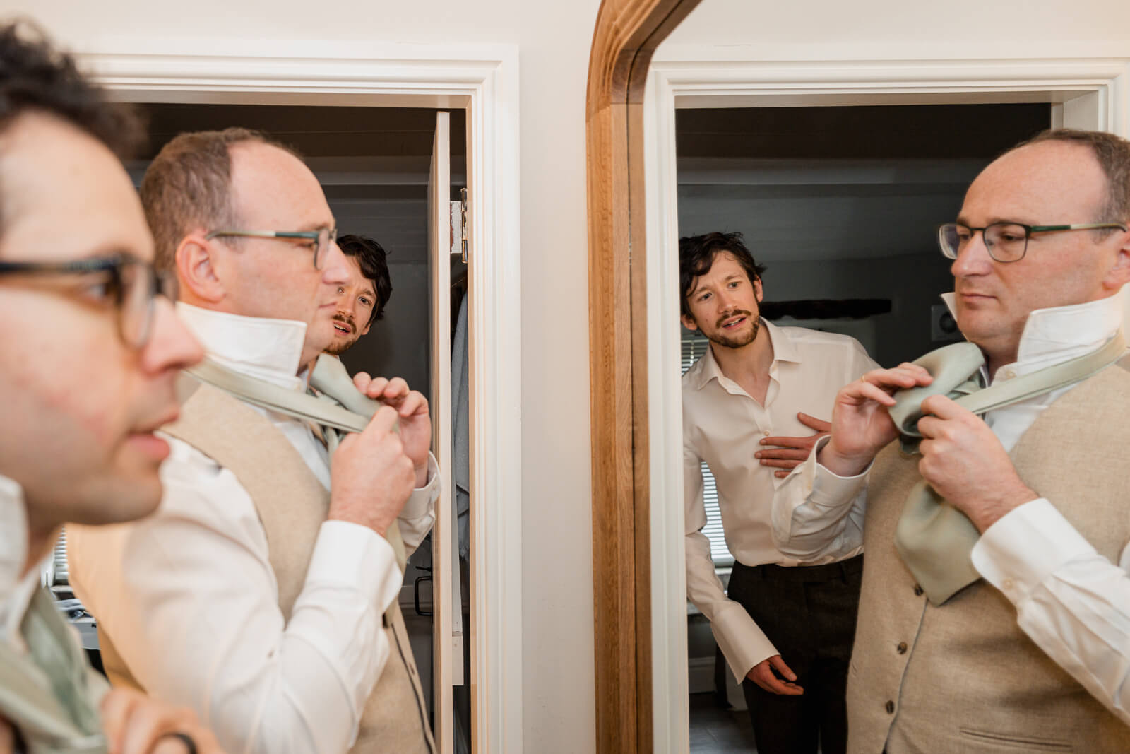 Groom getting ready at The Tithe Barn at Bolton Abbey adjusting tie in mirror with groomsmen