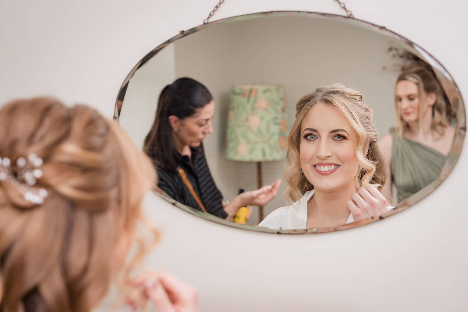 Bride smiling in mirror during wedding morning preparations with hair and makeup styling