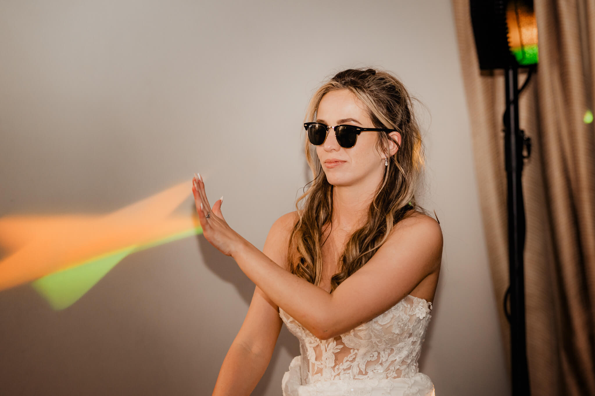 Bride in sunglasses playing with rainbow light during reception