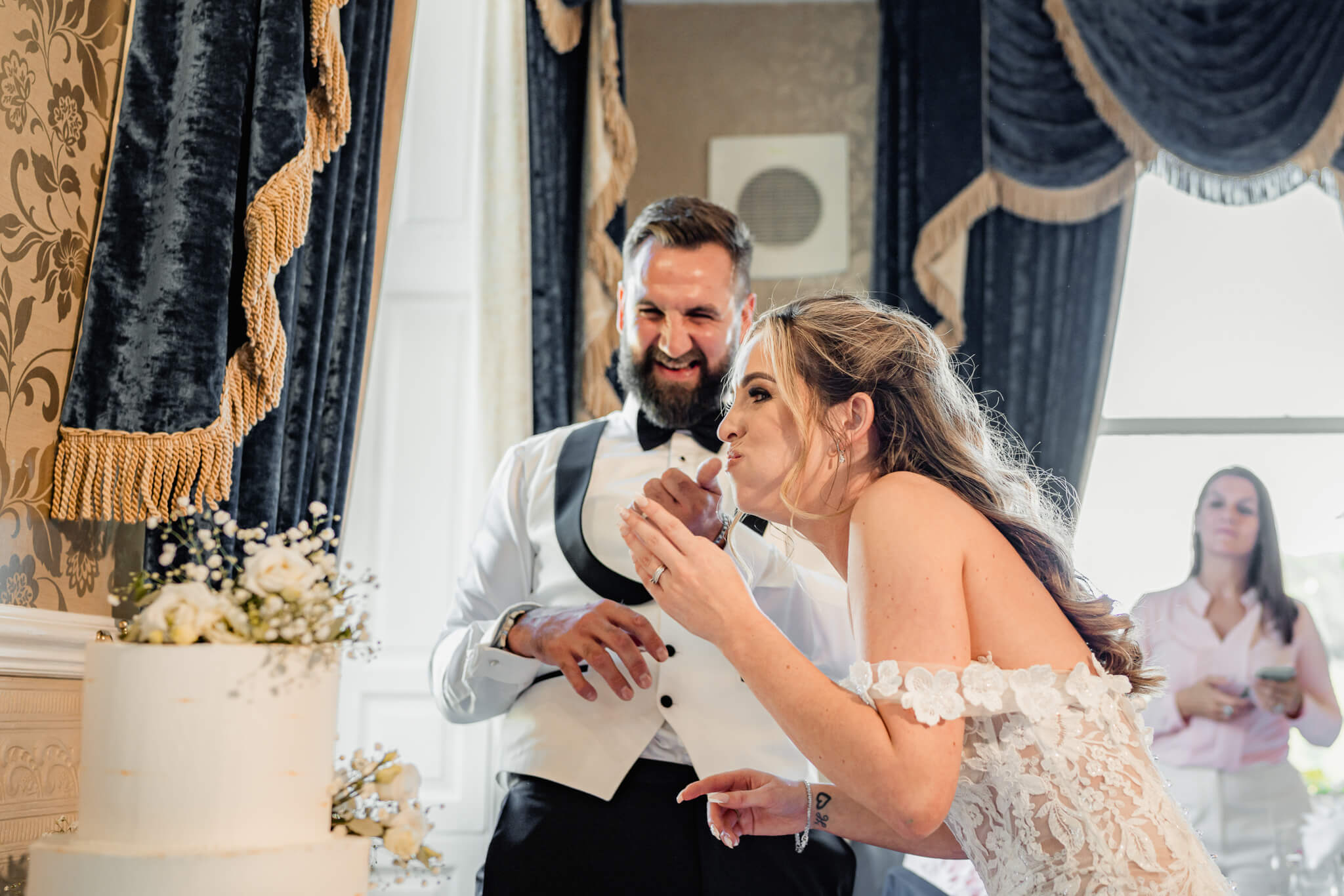 Bride playfully eating cake while groom laughs beside her