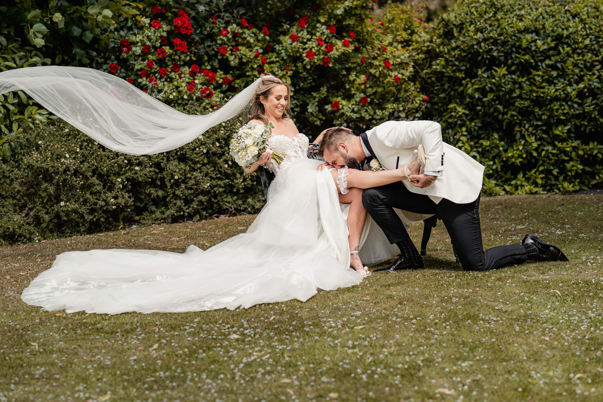 Groom kneeling and kissing bride’s hand as she laughs