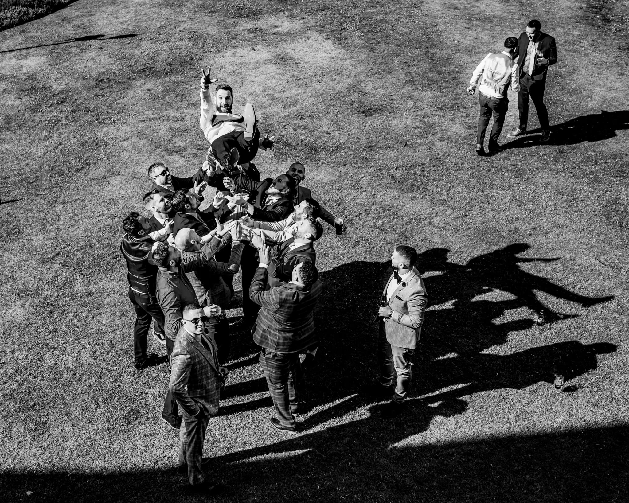 Groom being thrown in the air by groomsmen outdoors