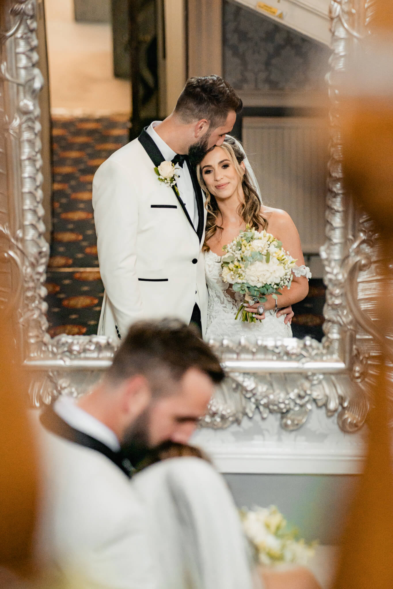 Bride and groom reflected in ornate mirror holding bouquet