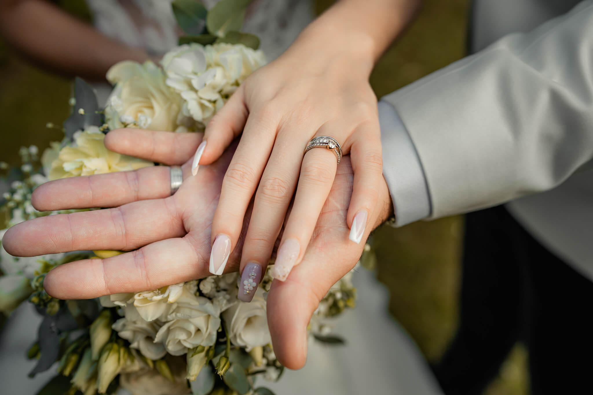 Bride and groom hands showing wedding rings over bouquet