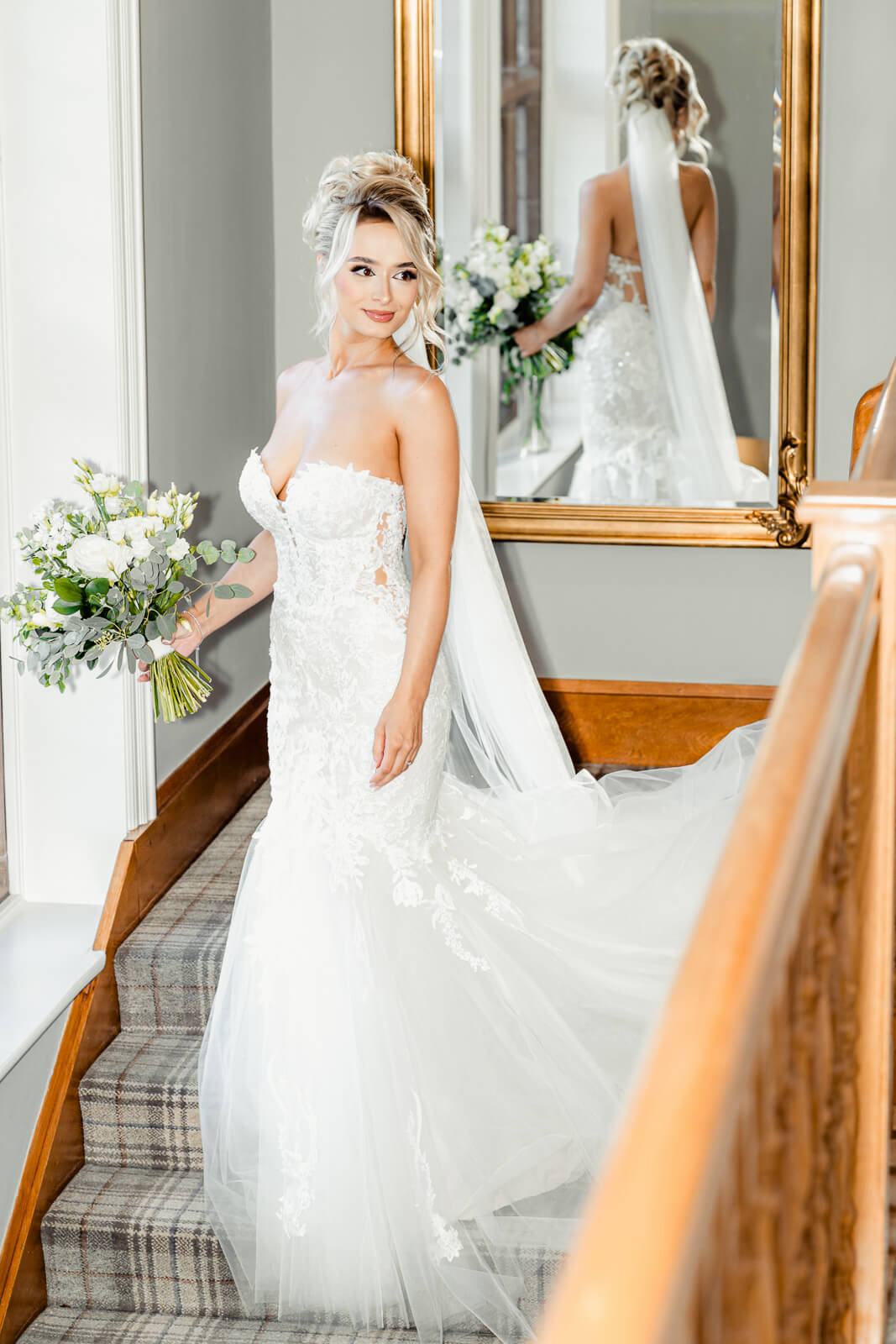 The bride holds her bouquet beside a window as her reflection appears in a mirror, creating a soft and romantic bridal portrait at Colshaw Hall Country Estate.