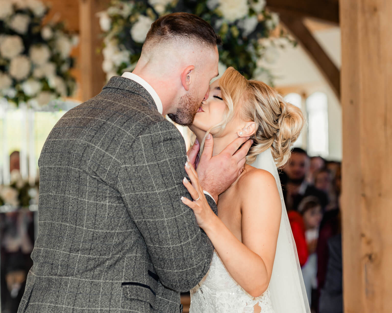 Bride and groom sharing a kiss during wedding ceremony with floral backdrop