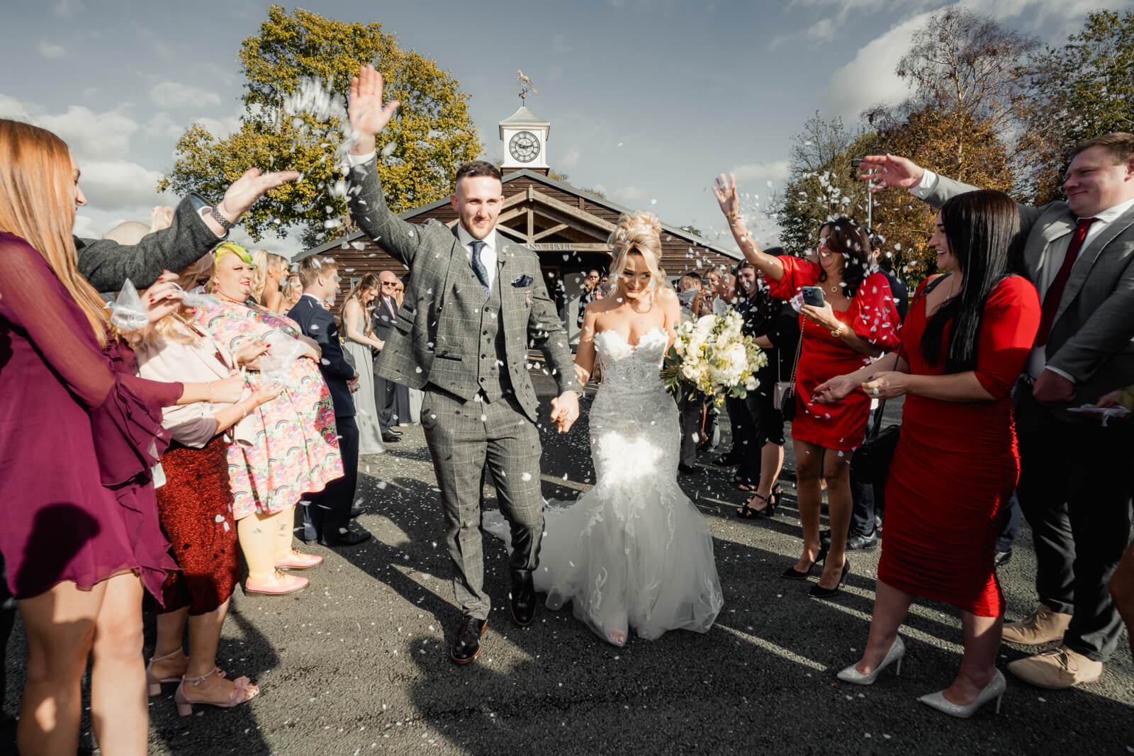 Bride and groom walking through confetti exit with guests cheering outside ceremony hall