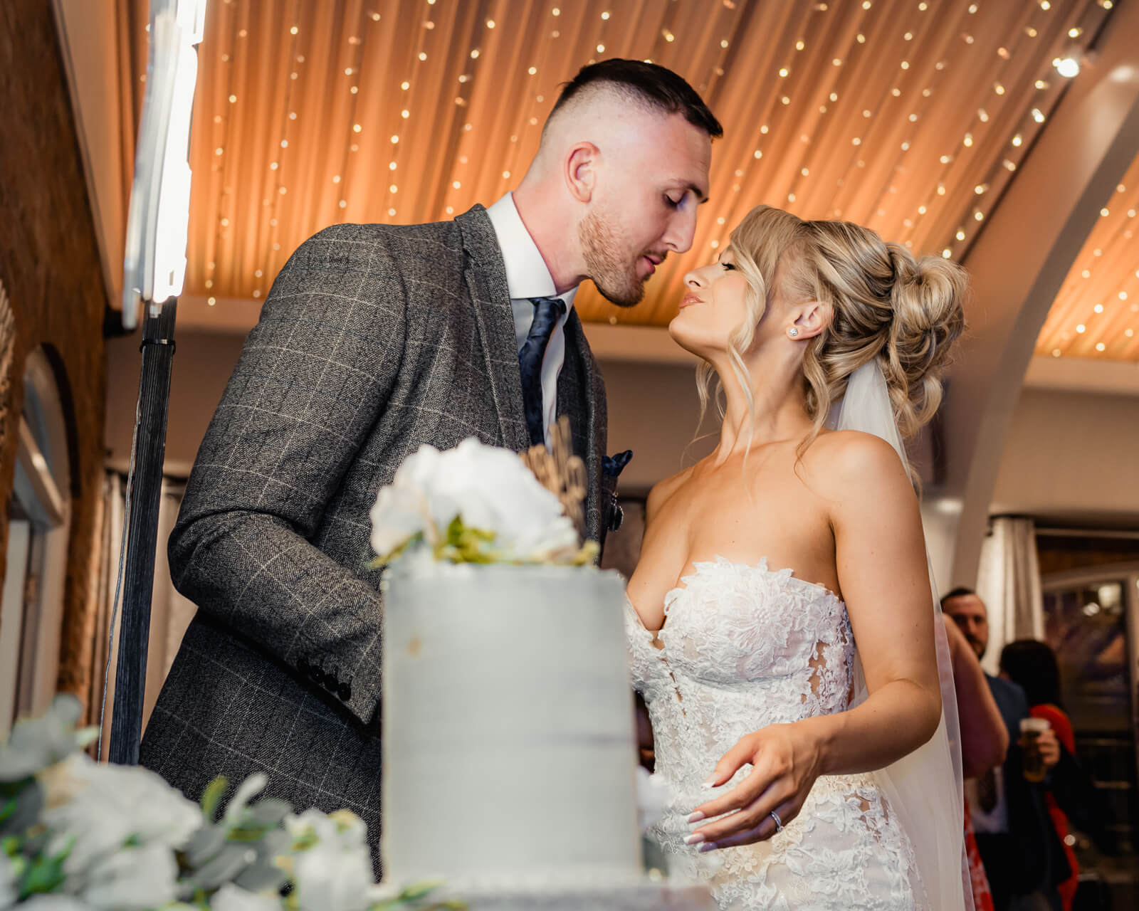 Bride and groom cutting wedding cake during Elegant Wedding at Colshaw Hall Country Estate with warm reception lighting