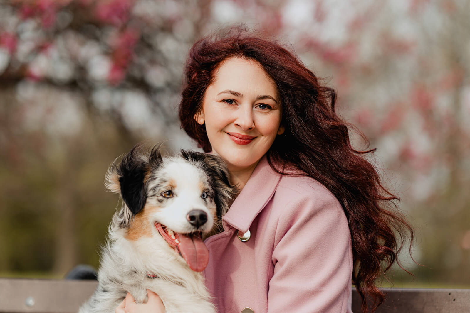 close-up portrait of a woman holding her dog under pink blossoms