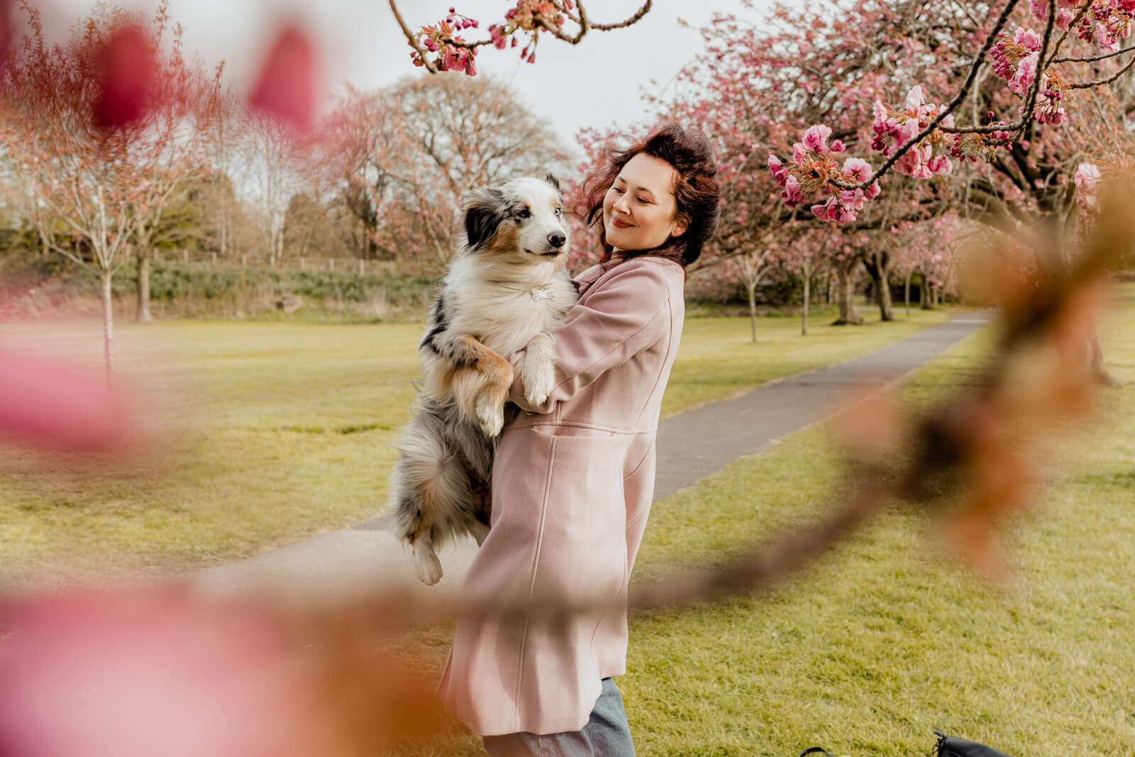 woman playfully lifting her dog outdoors under pink blossoms