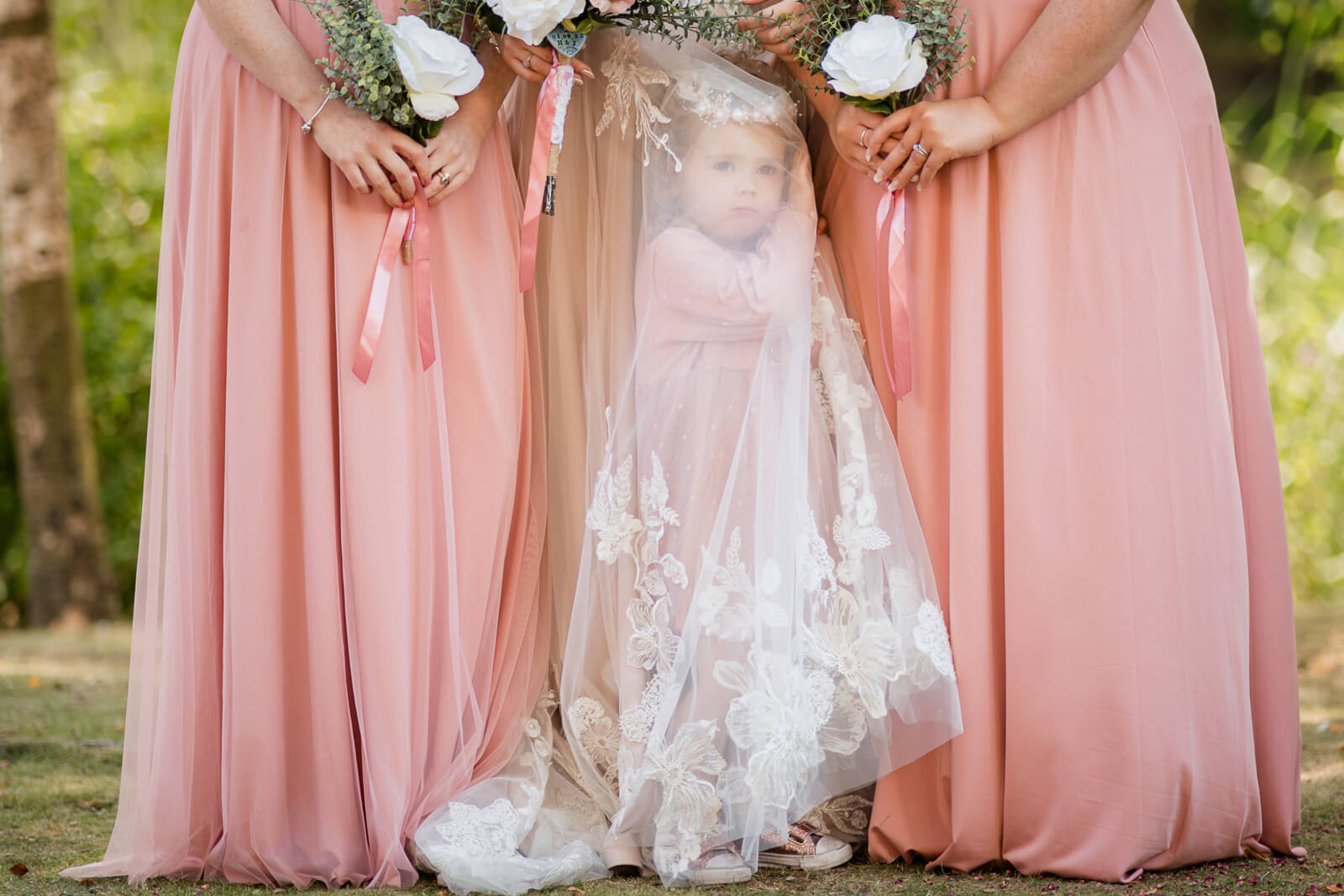 Flower girl standing between bridesmaids in blush dresses holding bouquets