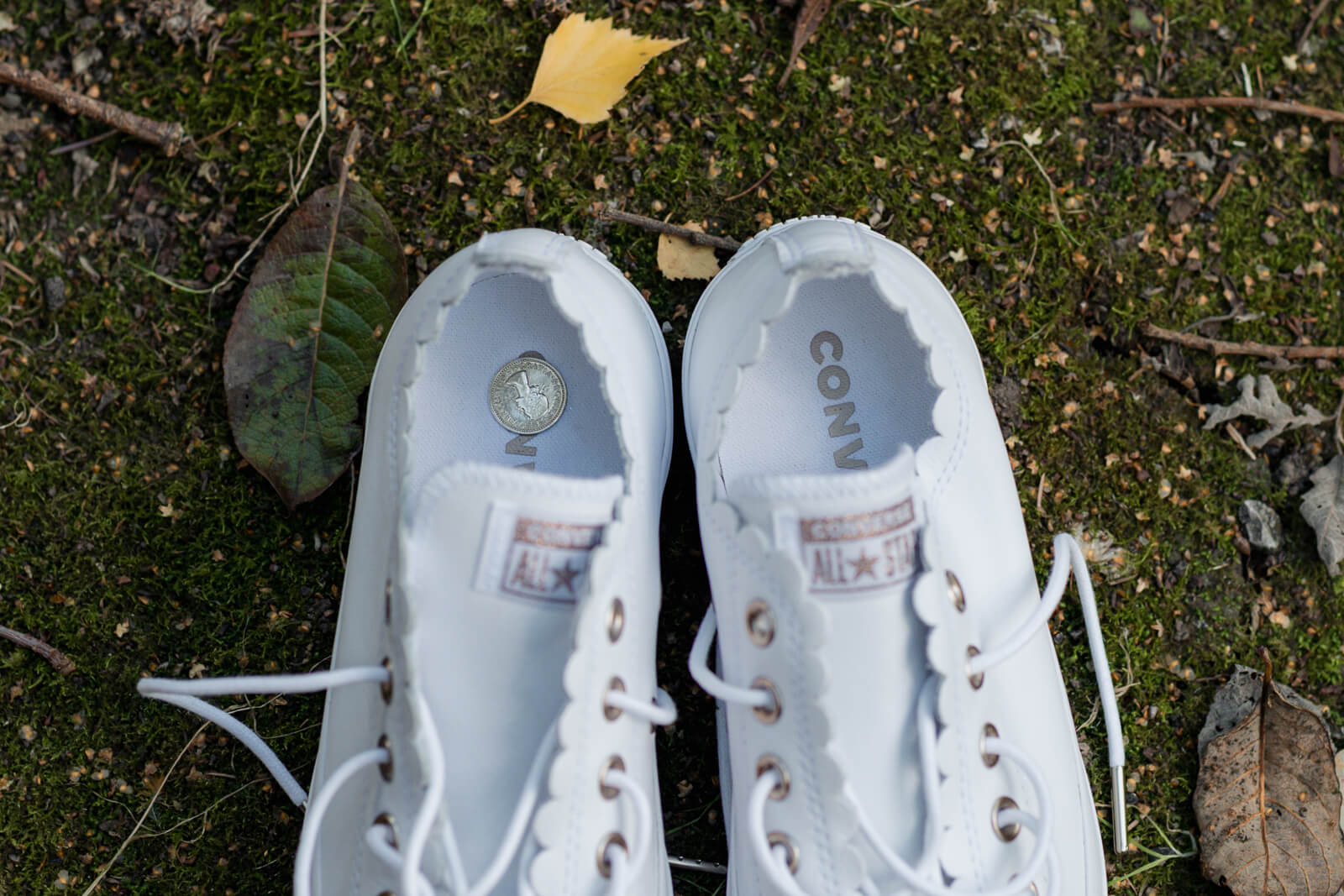 White wedding shoes with a coin placed inside on mossy ground
