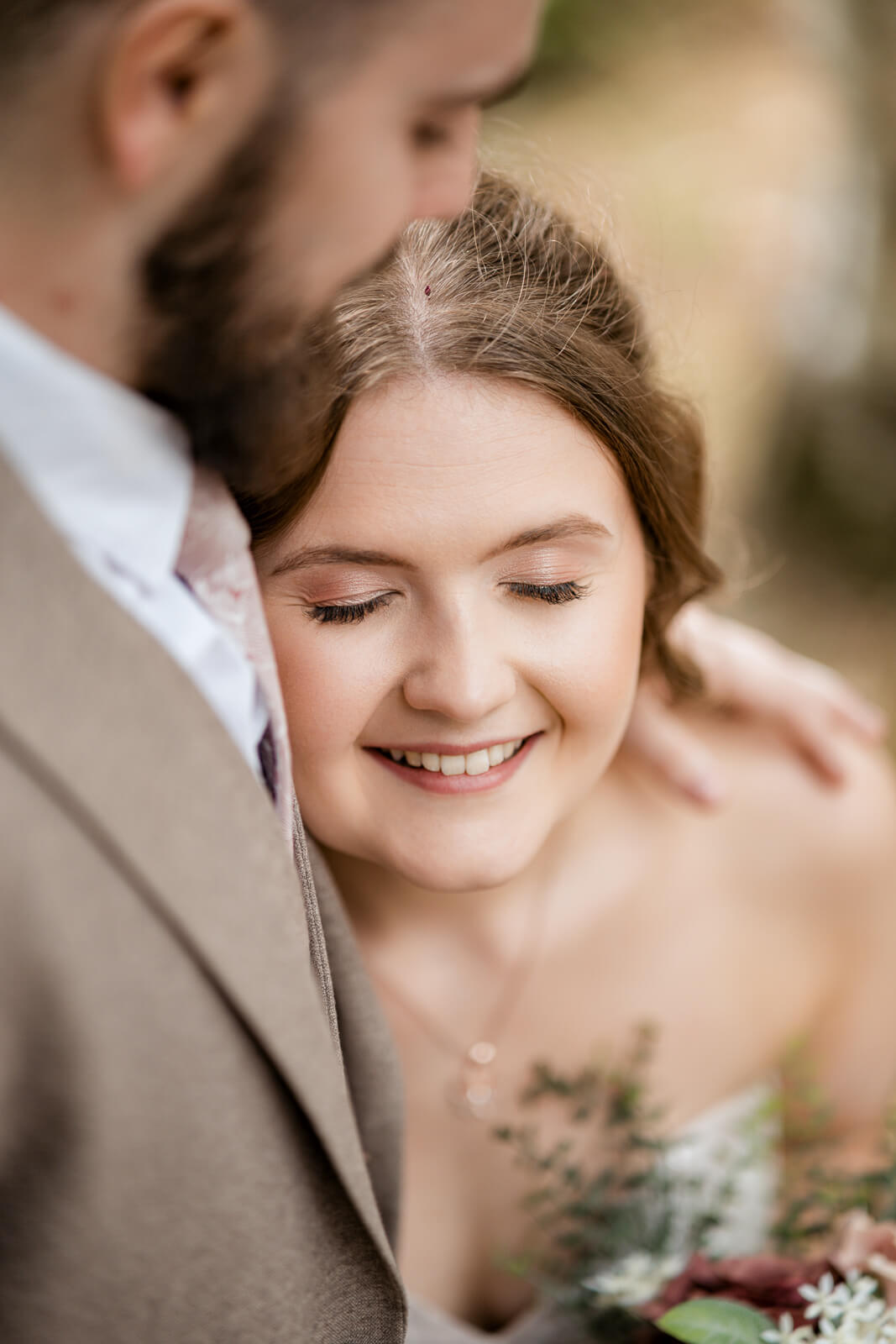 Bride smiling with eyes closed leaning against groom