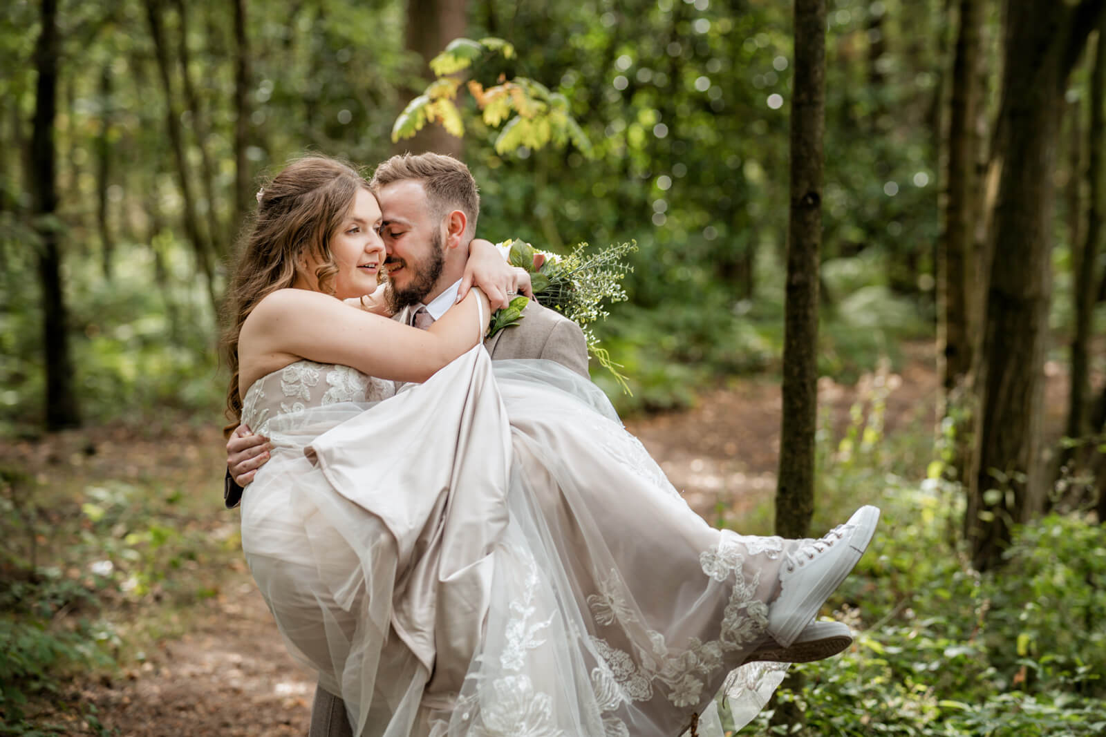 Groom carrying bride in forest at Chevin Country Park wedding
