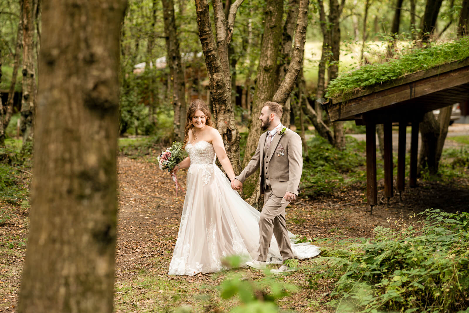 Bride and groom walking through woodland at Chevin Country Park wedding venue