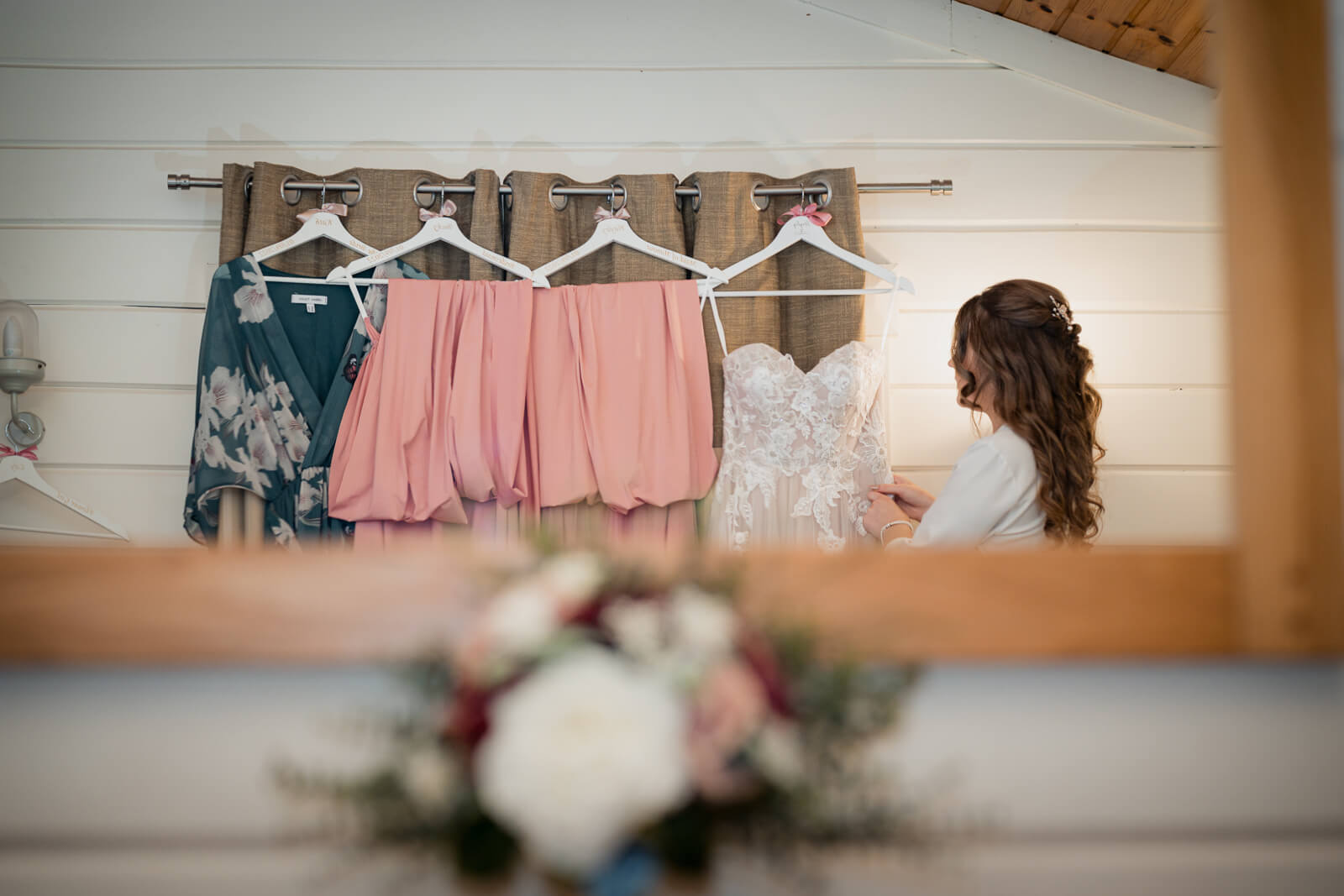 Bride looking at wedding dress and bridesmaid dresses hanging on a rail