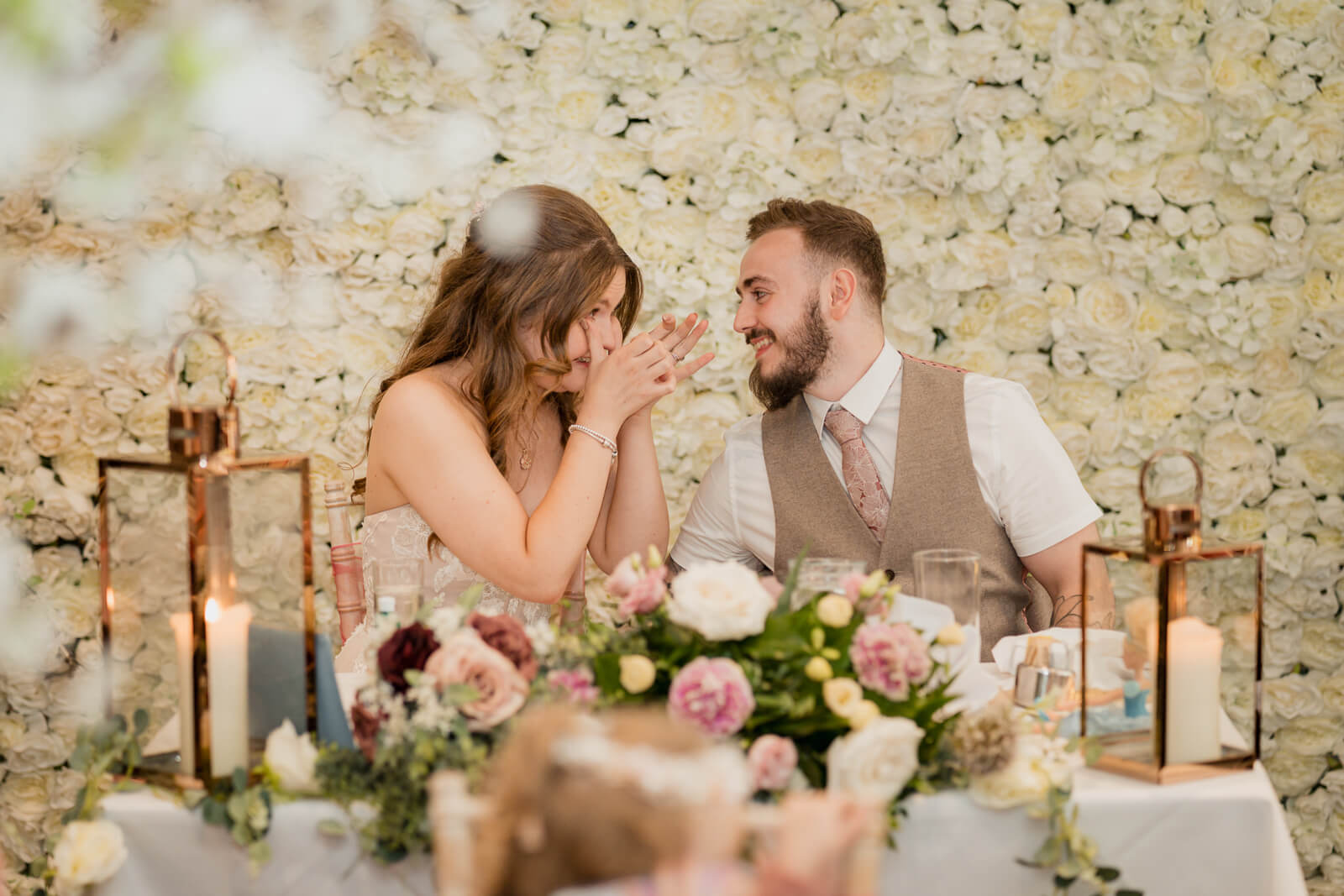 Bride and groom laughing at reception table with floral backdrop at Chevin Country Park